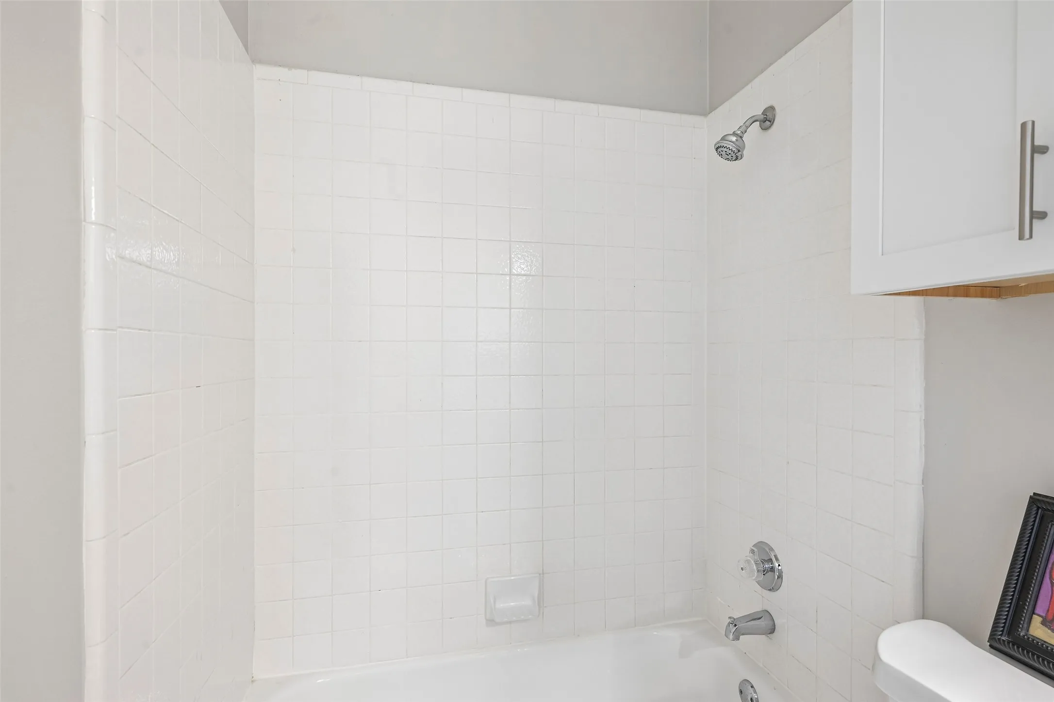 Tub and shower combination featuring white square tile surround, chrome showerhead, and chrome tub filler