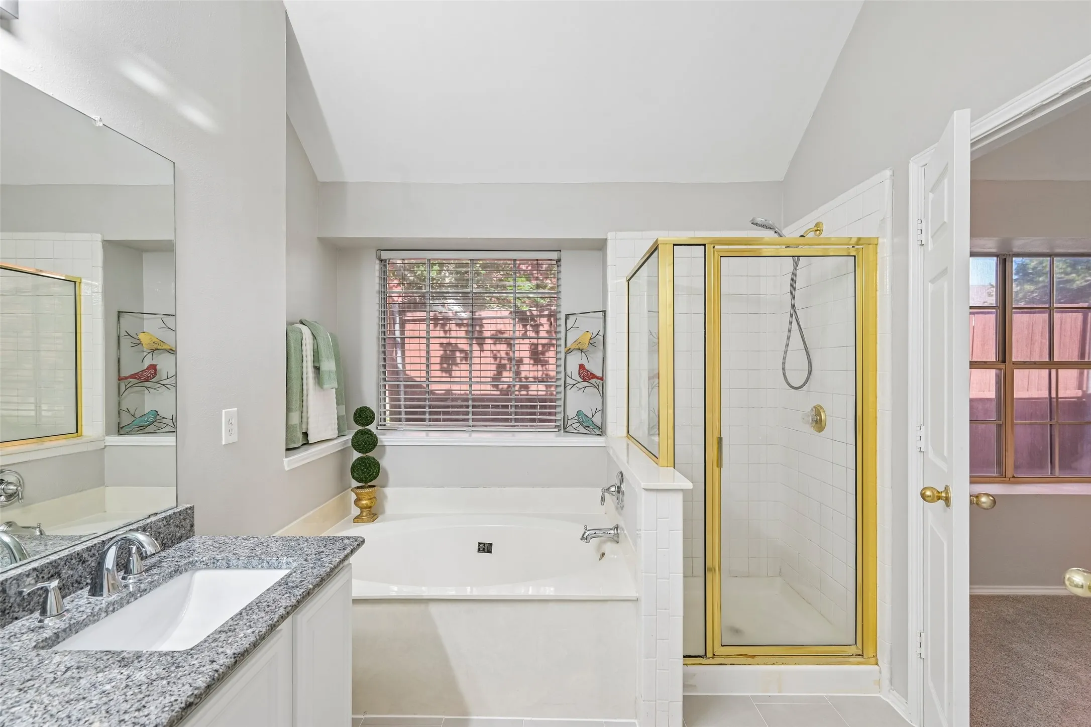 Built-in soaking tub, walk-in shower with gold-finish frame, single vanity with granite-style countertop, and integrated sink