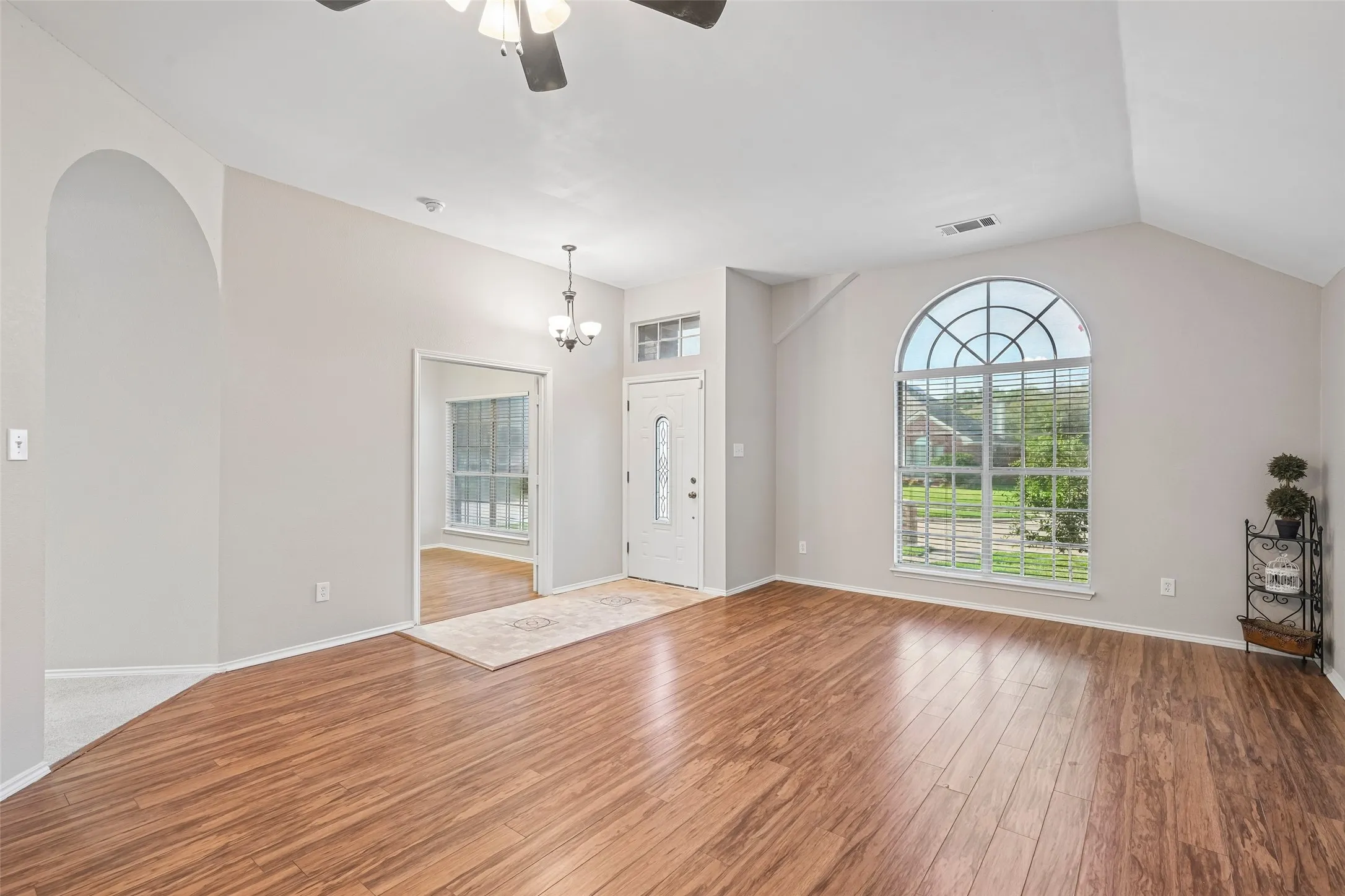 Spacious living area featuring gleaming laminate flooring, vaulted ceilings with ceiling fan, and an arched transom window framing natural light