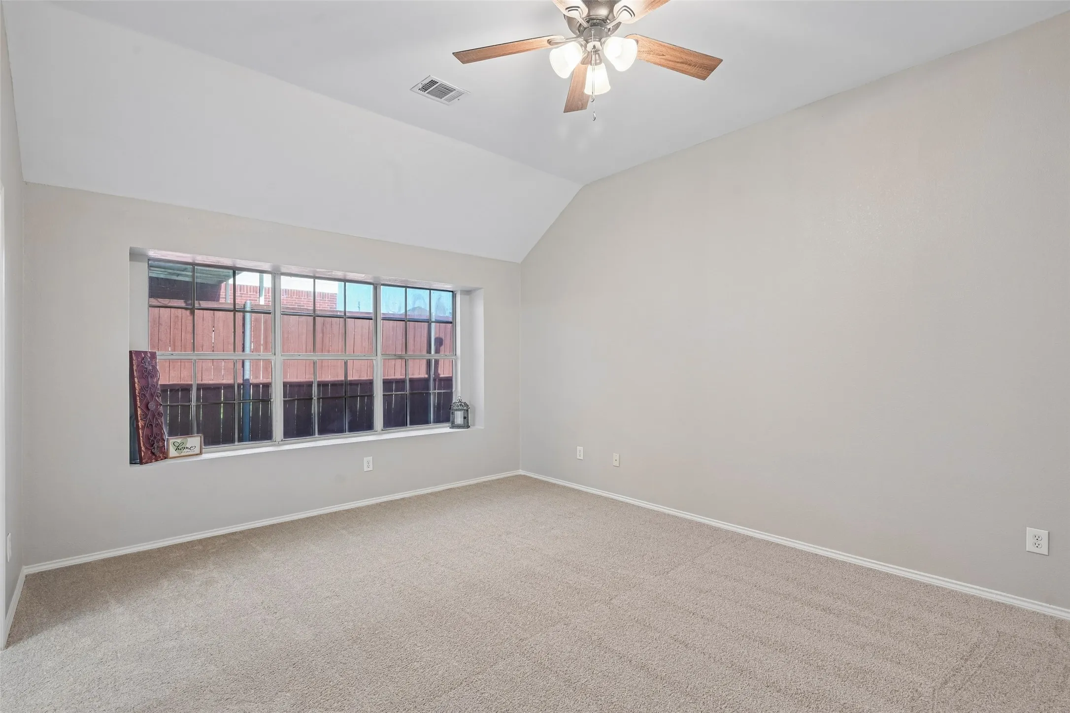 Vaulted ceiling, ceiling fan with light fixture, neutral-tone carpeting, large window with deep sill, light gray wall finishes