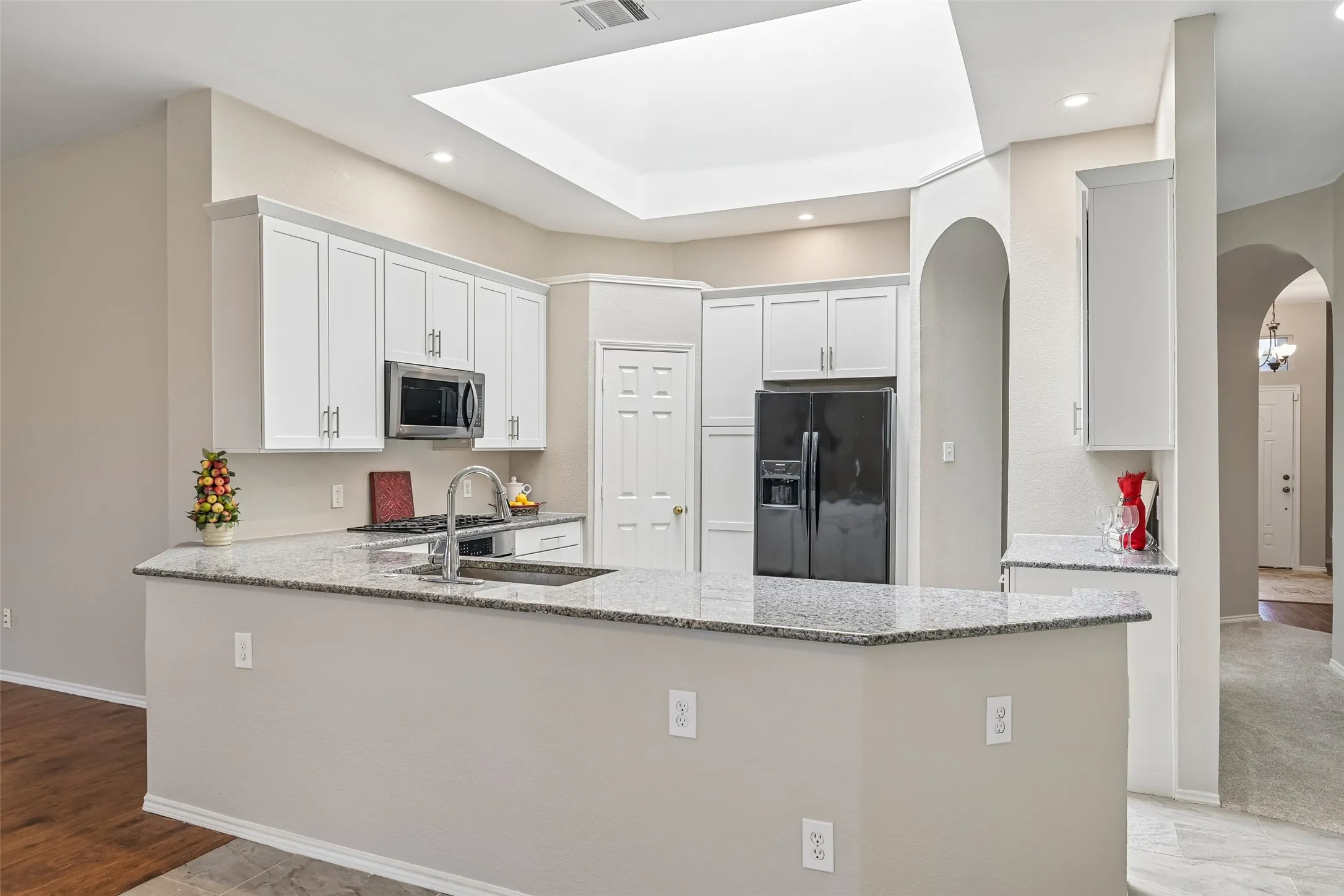 Kitchen featuring white cabinetry, stainless steel microwave, black refrigerator, granite countertops, and recessed lighting