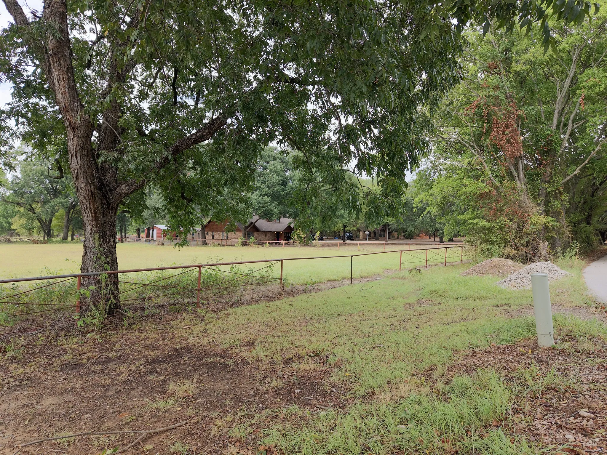 Expansive green space with mature trees, perimeter fencing, and a rustic structure in the background