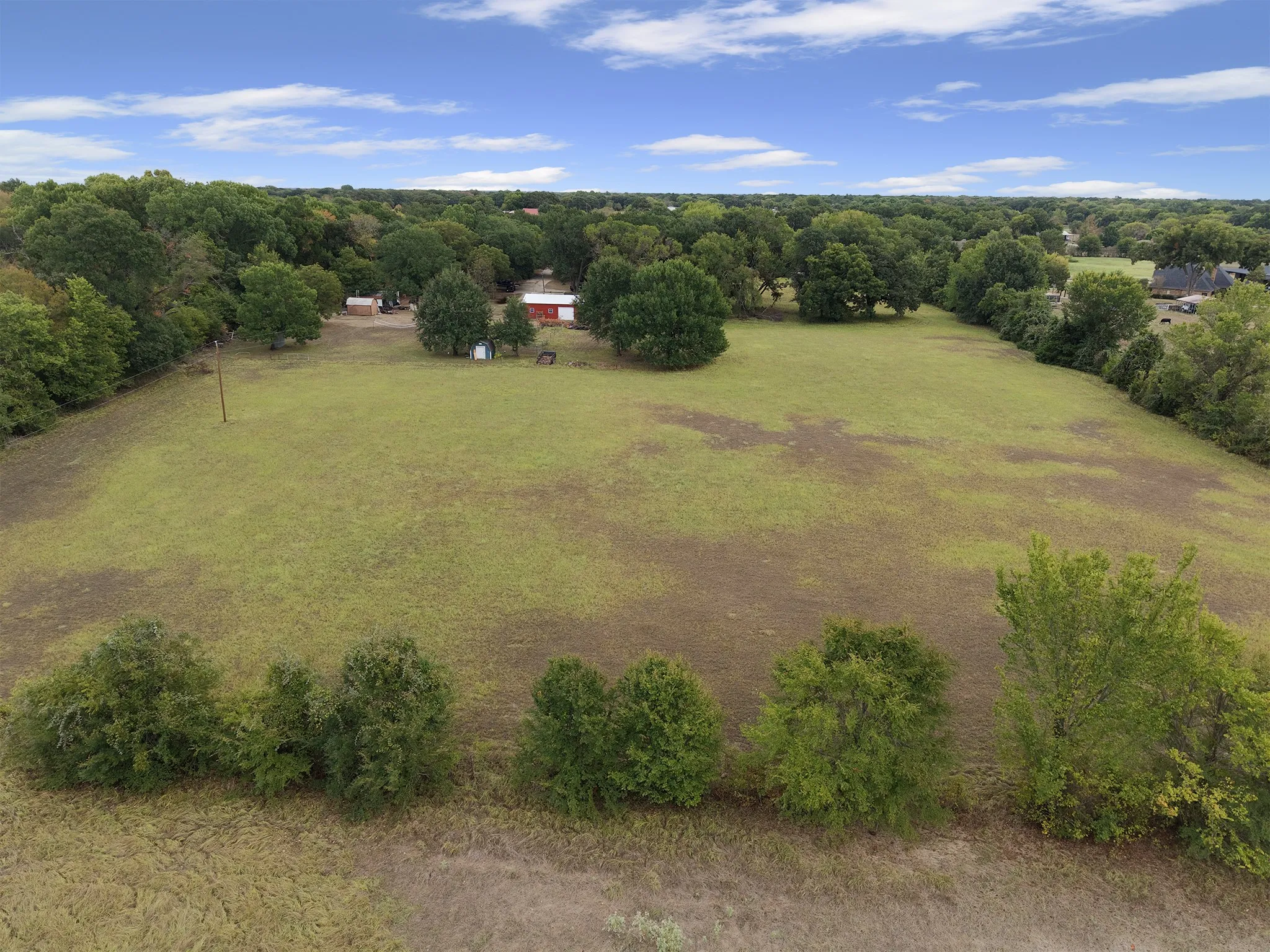 Expansive green space with scattered trees and a distant red structure