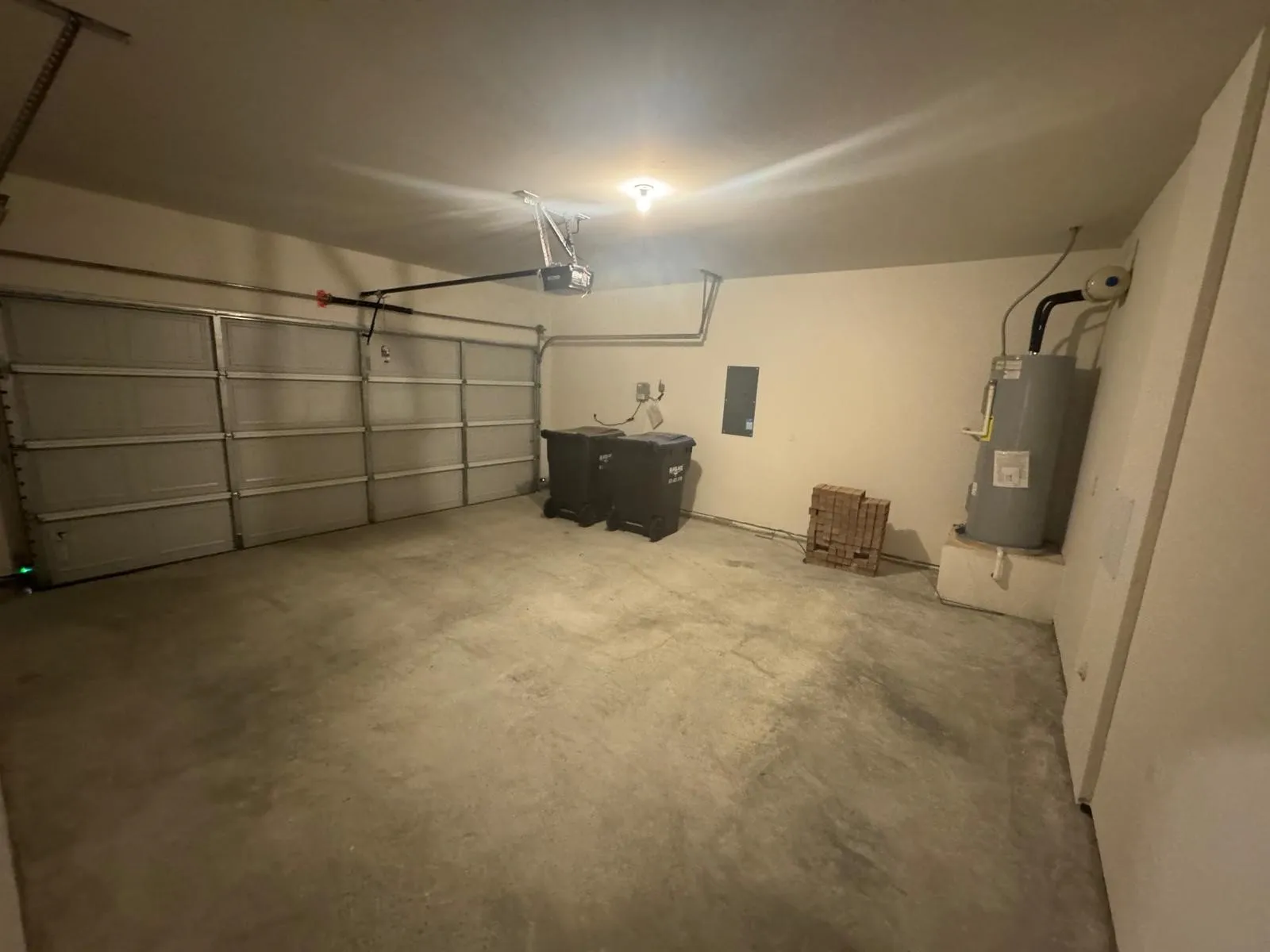 Garage with water heater, electric panel, and a garage door opener