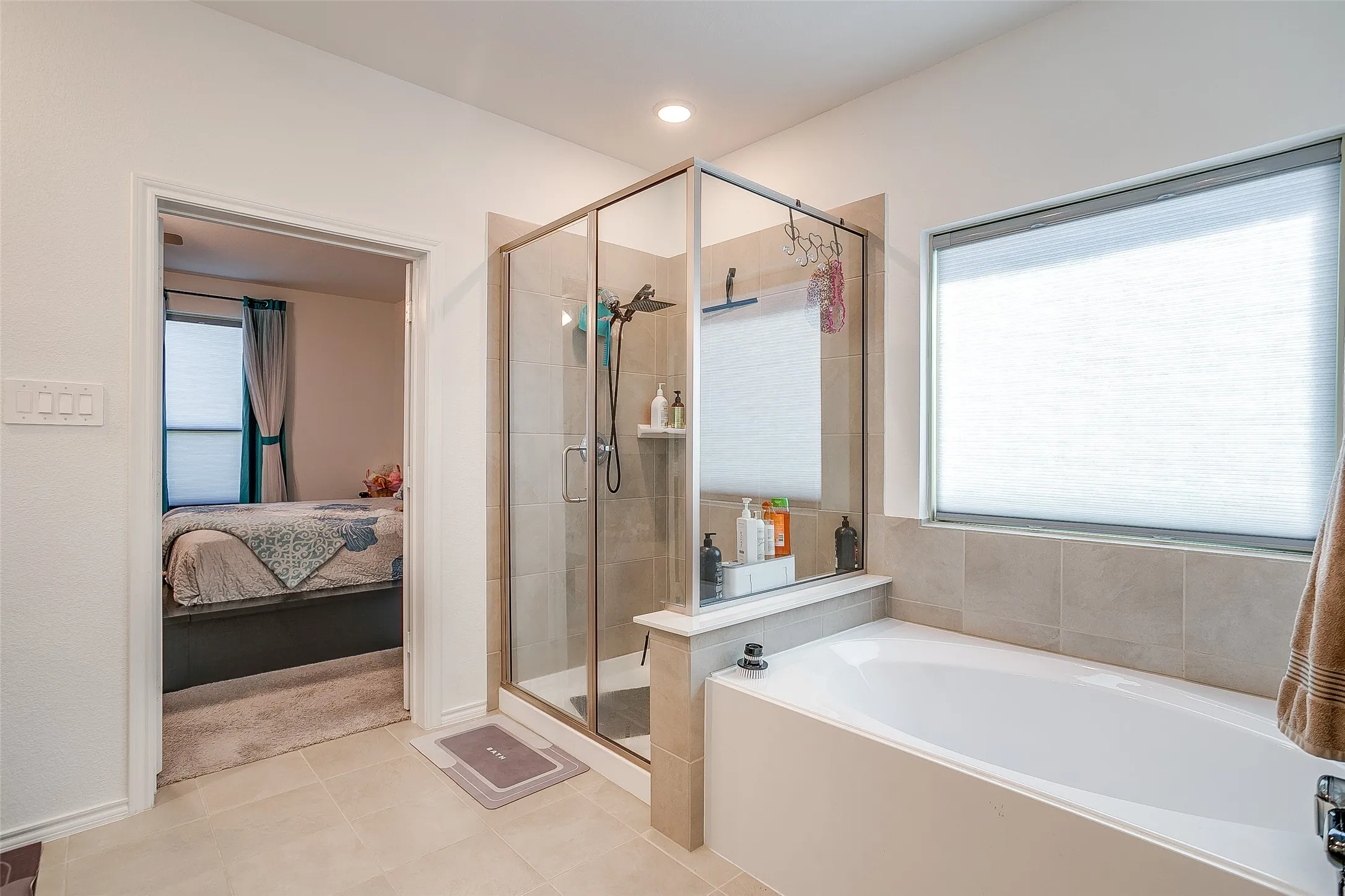 Full-size bathtub with a tiled surround, glass-enclosed shower, and neutral-toned wall and floor tile