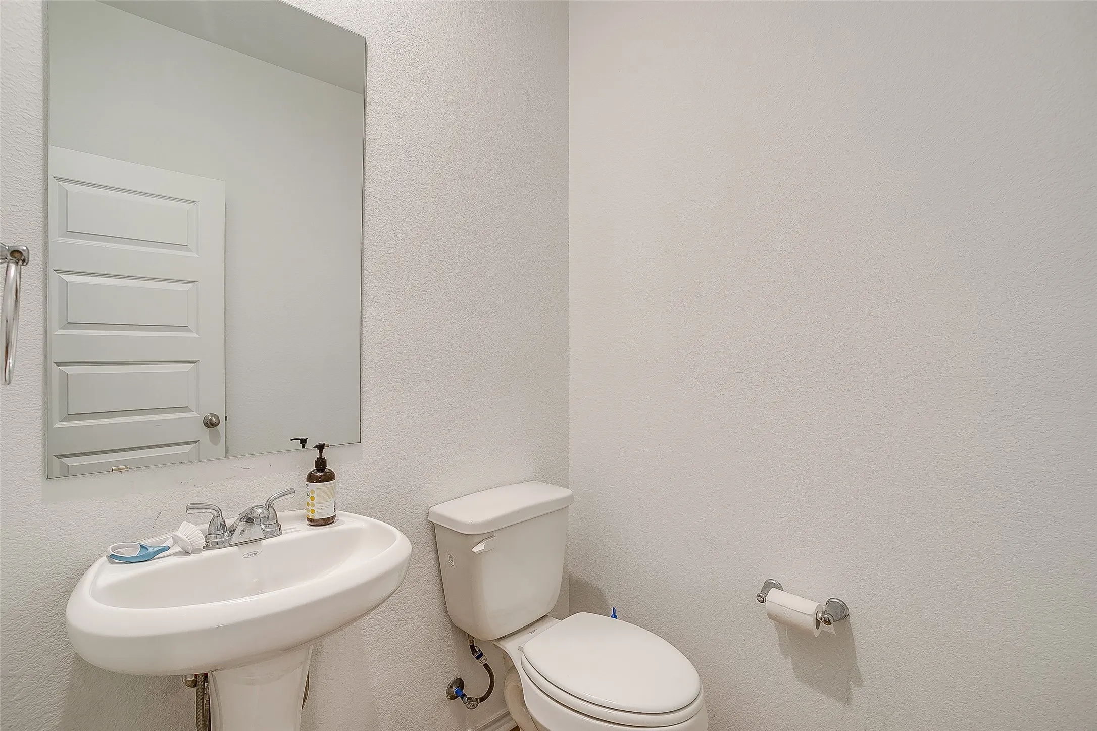 Pedestal sink with chrome faucet, wall-mounted mirror, and white paneled door