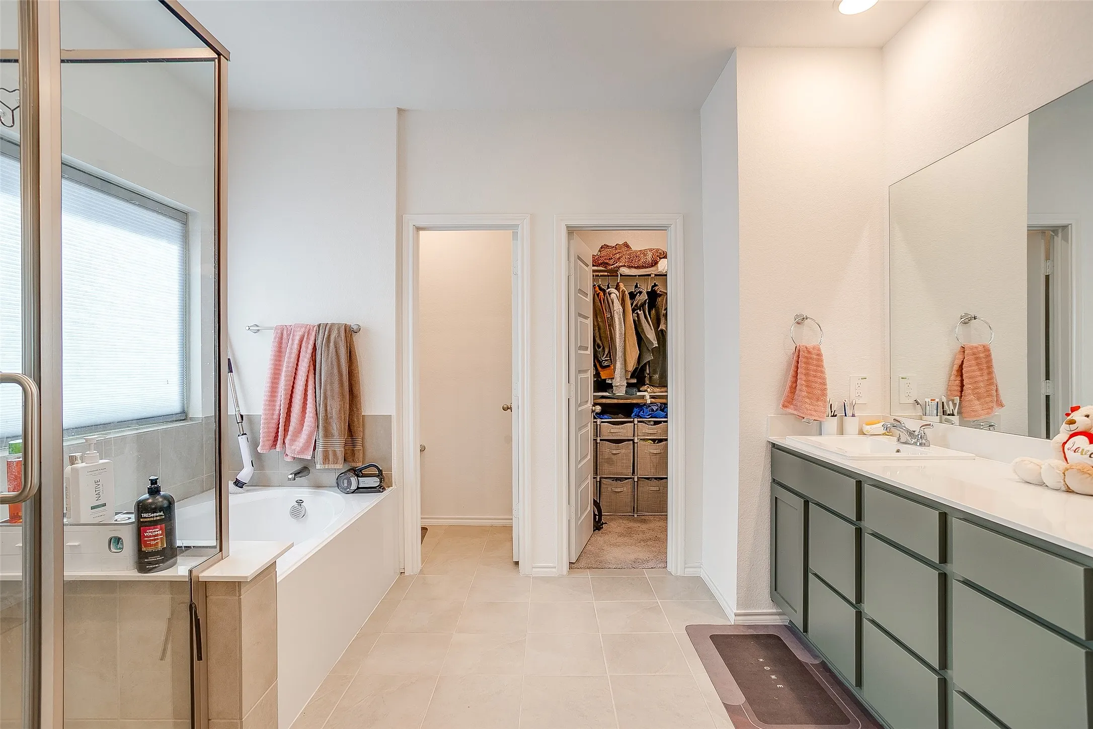 Spacious bathroom featuring a built-in bathtub, glass-enclosed shower, dual vanity with a large mirror, and tiled flooring