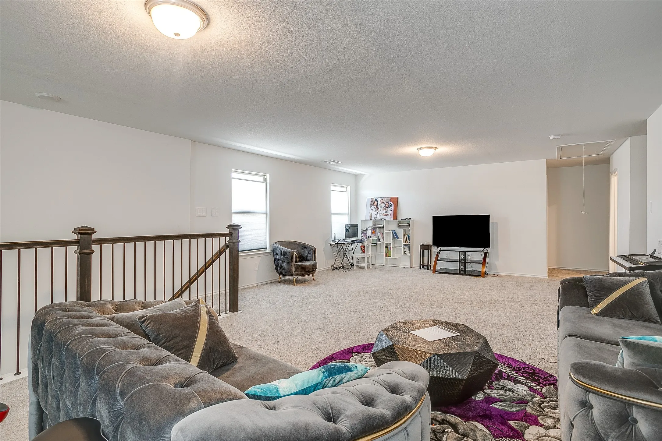 Expansive carpeted area with neutral walls, recessed lighting, and a dark wood and metal railing