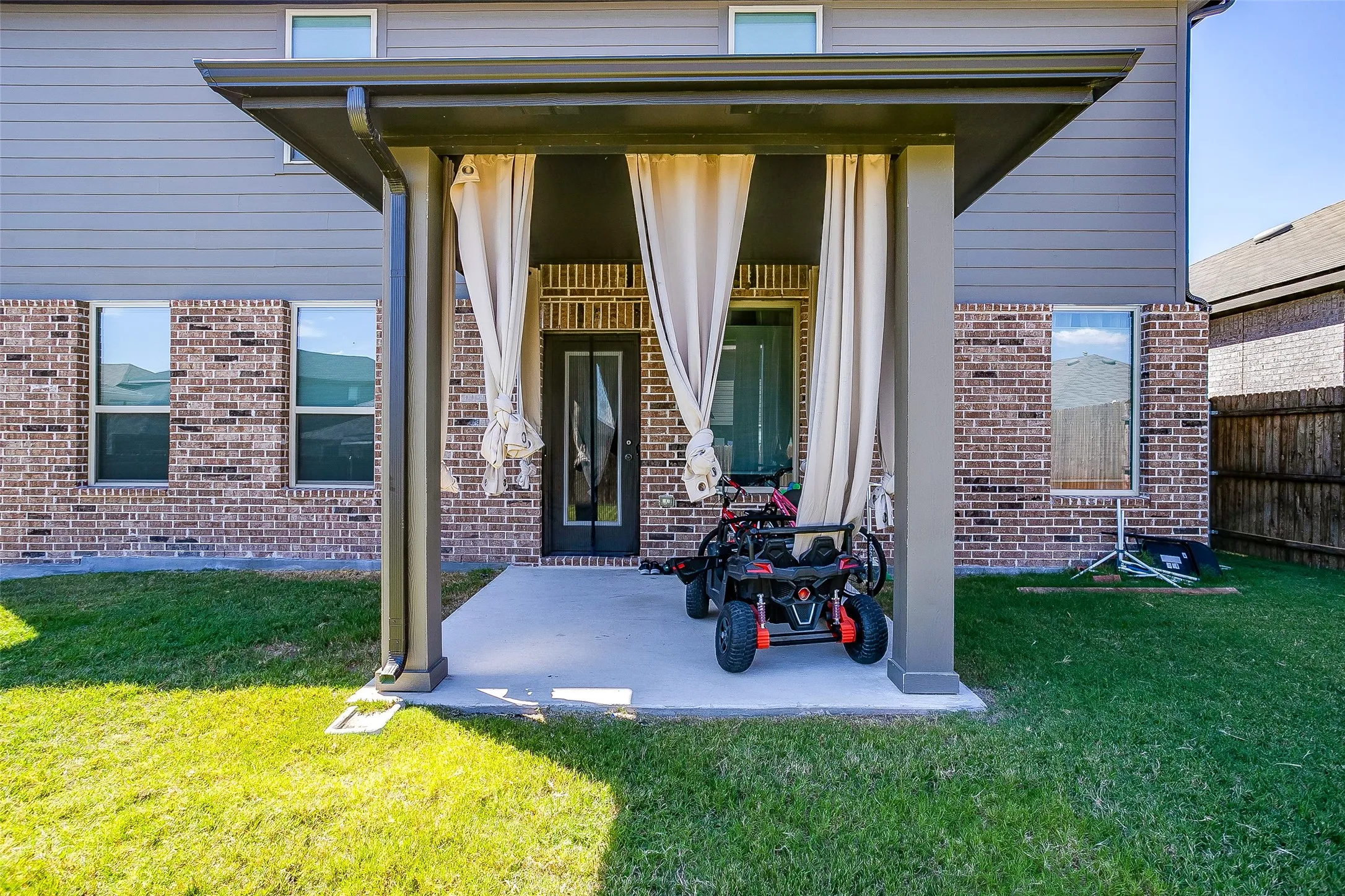 Covered patio with a concrete slab, featuring a dark-framed glass paneled door and brick exterior