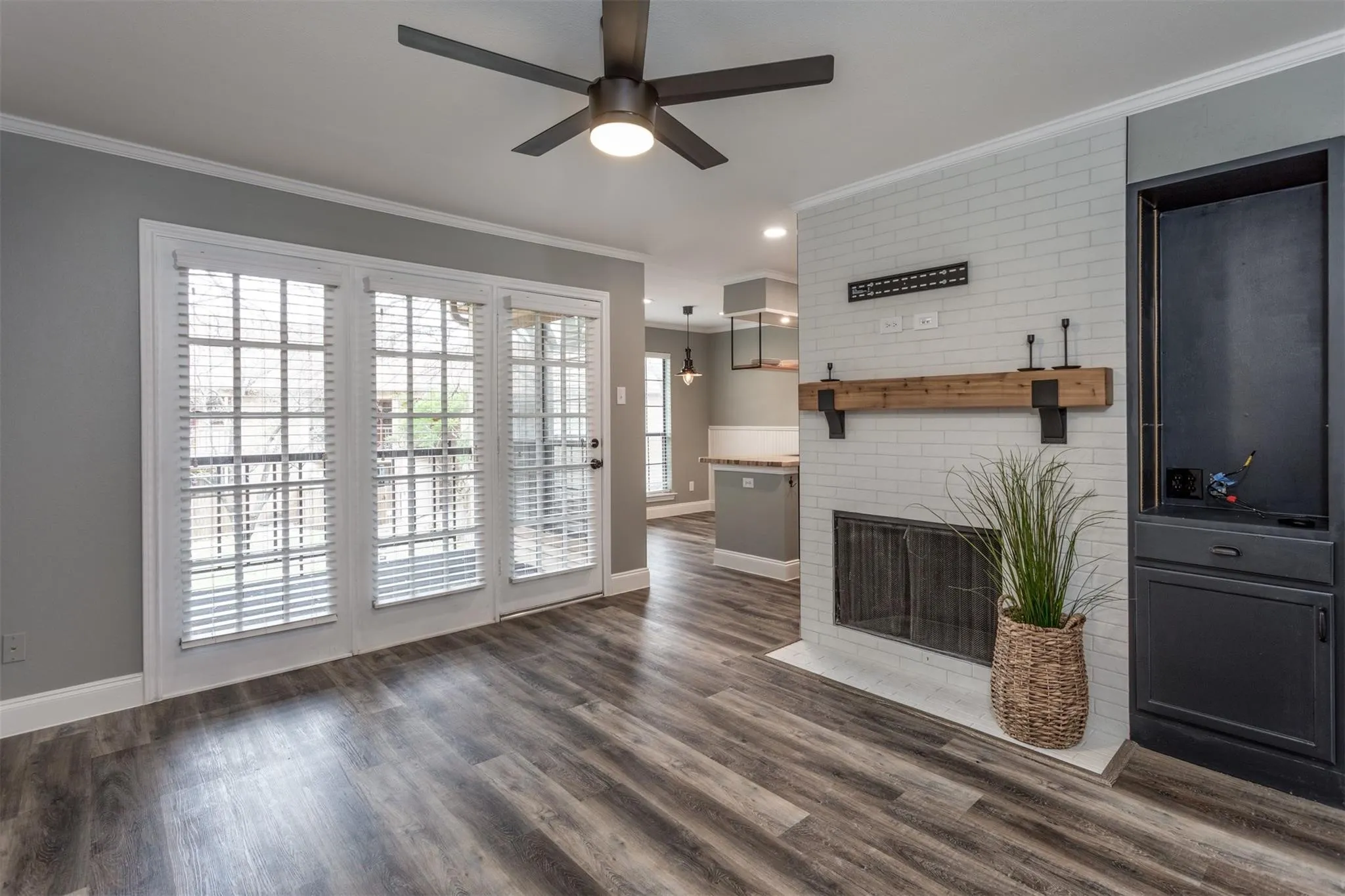 Living room with ceiling fan and wood-like floors has lots of natural lighting and French style doors, wood burning fireplace that has a decorative mantle.