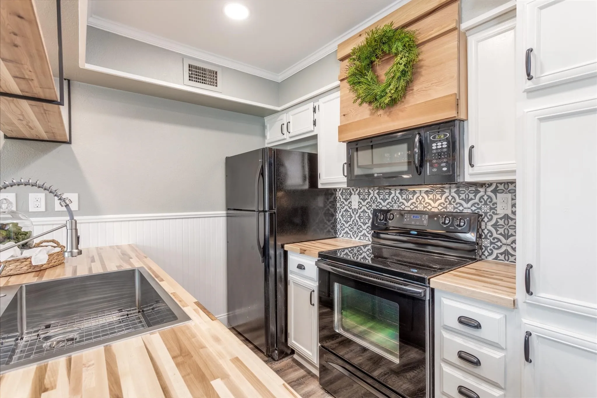 Butcher block countertops, farm sink, open cabinet at peninsula, Electric range, microwave, and refrigerator.