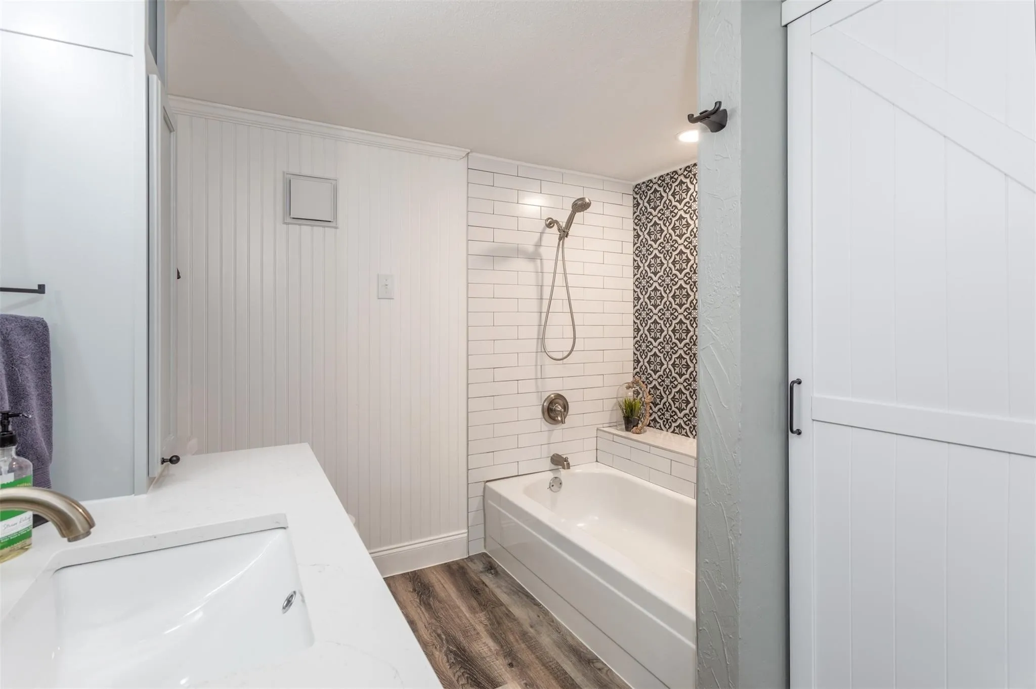Bathroom equipped with sink, tub/shower combo, wood-like flooring.