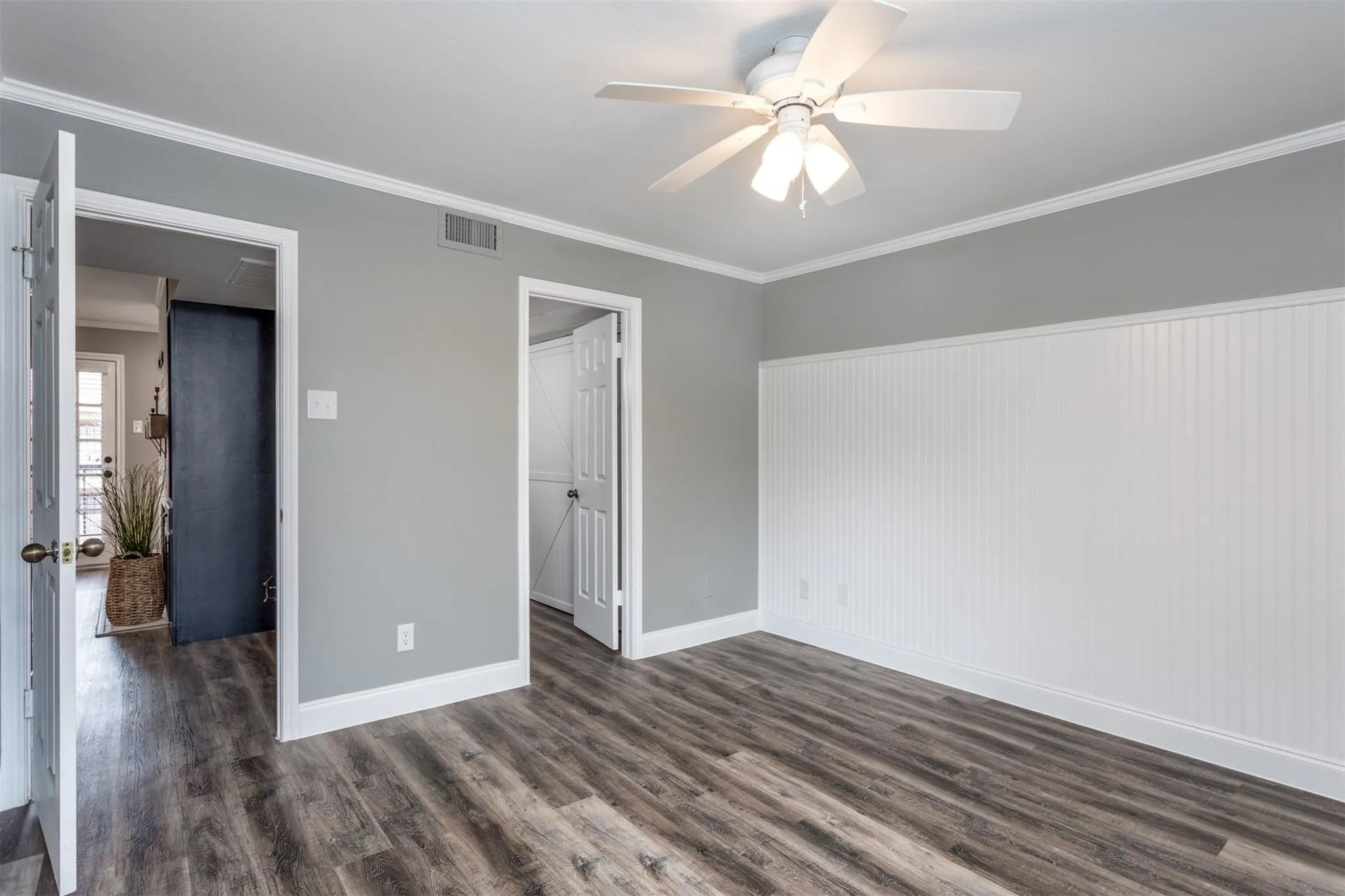 Generous sized bedroom with light gray walls, wood-like flooring and ceiling fan.  Bead-board decorative wall.  Ensuite to bathroom.