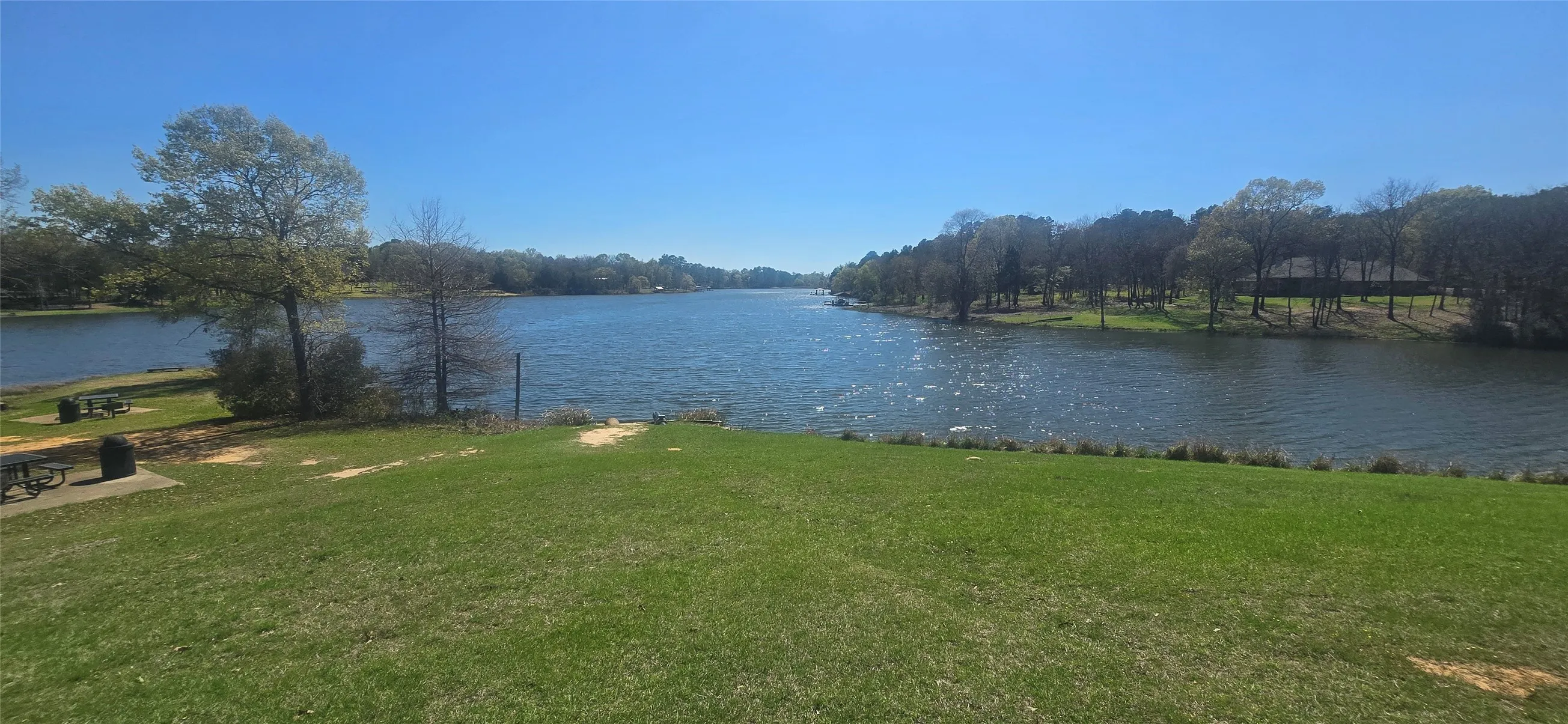 Expansive waterfront property featuring a wide lake frontage, surrounding mature trees, and a manicured lawn