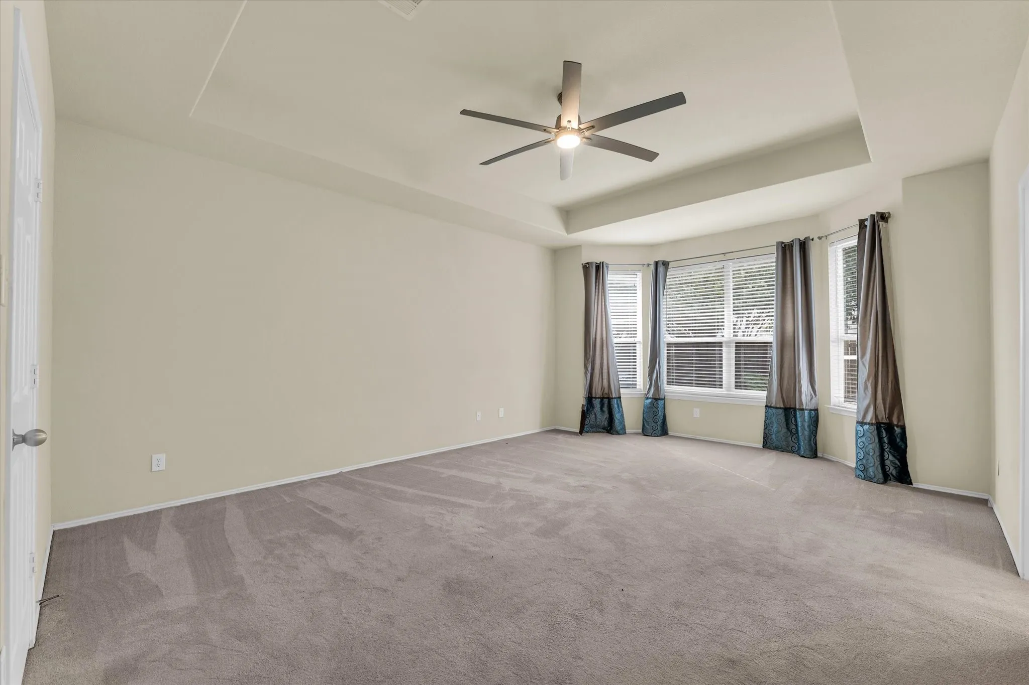 Tray ceiling with a ceiling fan, bay windows with blinds, and neutral carpet flooring