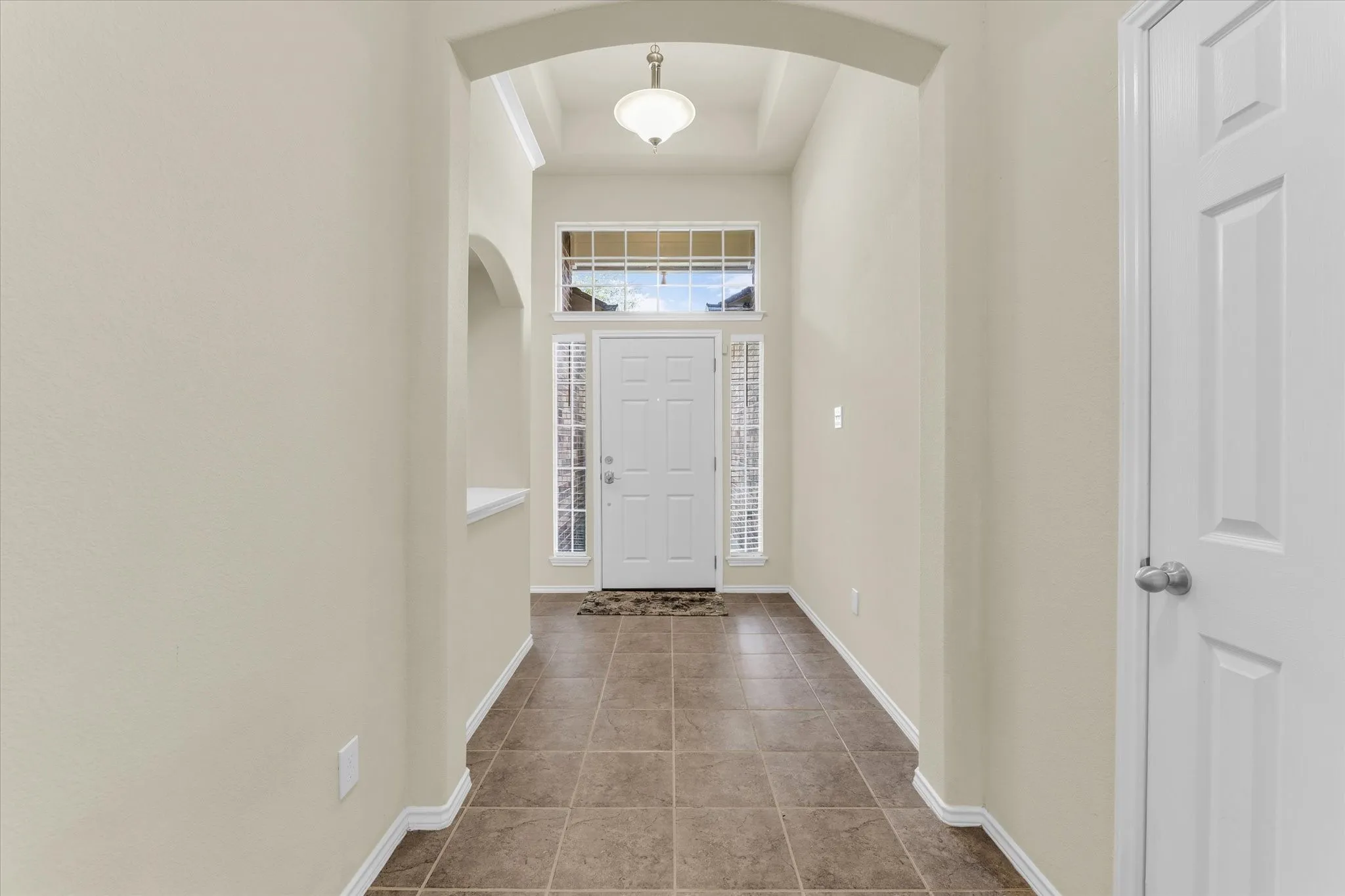 Entryway featuring tiled flooring, an arched doorway, and a white paneled door with sidelights and a transom window