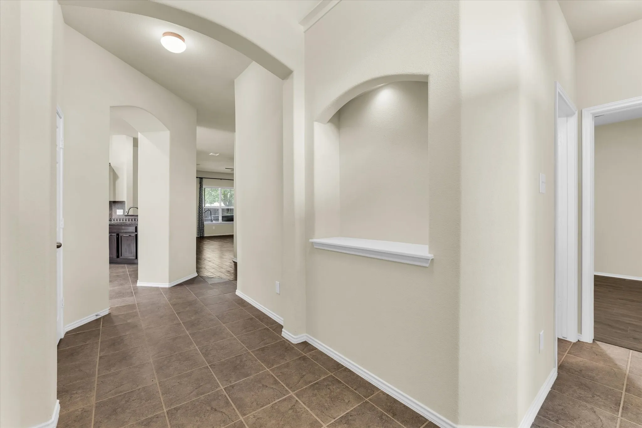 Arched wall openings, recessed wall niche with accent lighting, tile flooring, and light wall finishes