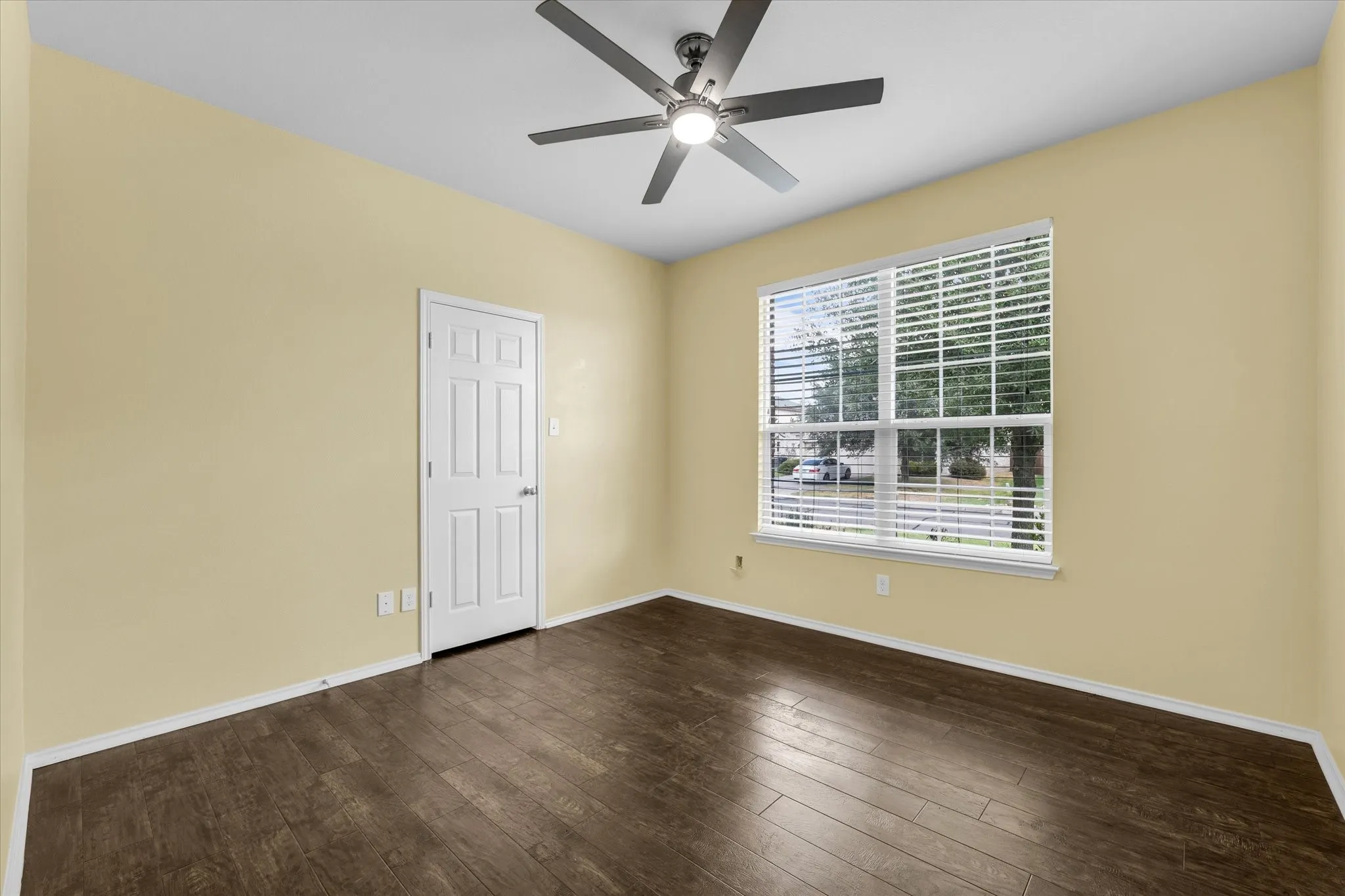 Room featuring wood-finish flooring, a ceiling fan with integrated lighting, a multi-pane window with blinds, and a paneled interior door