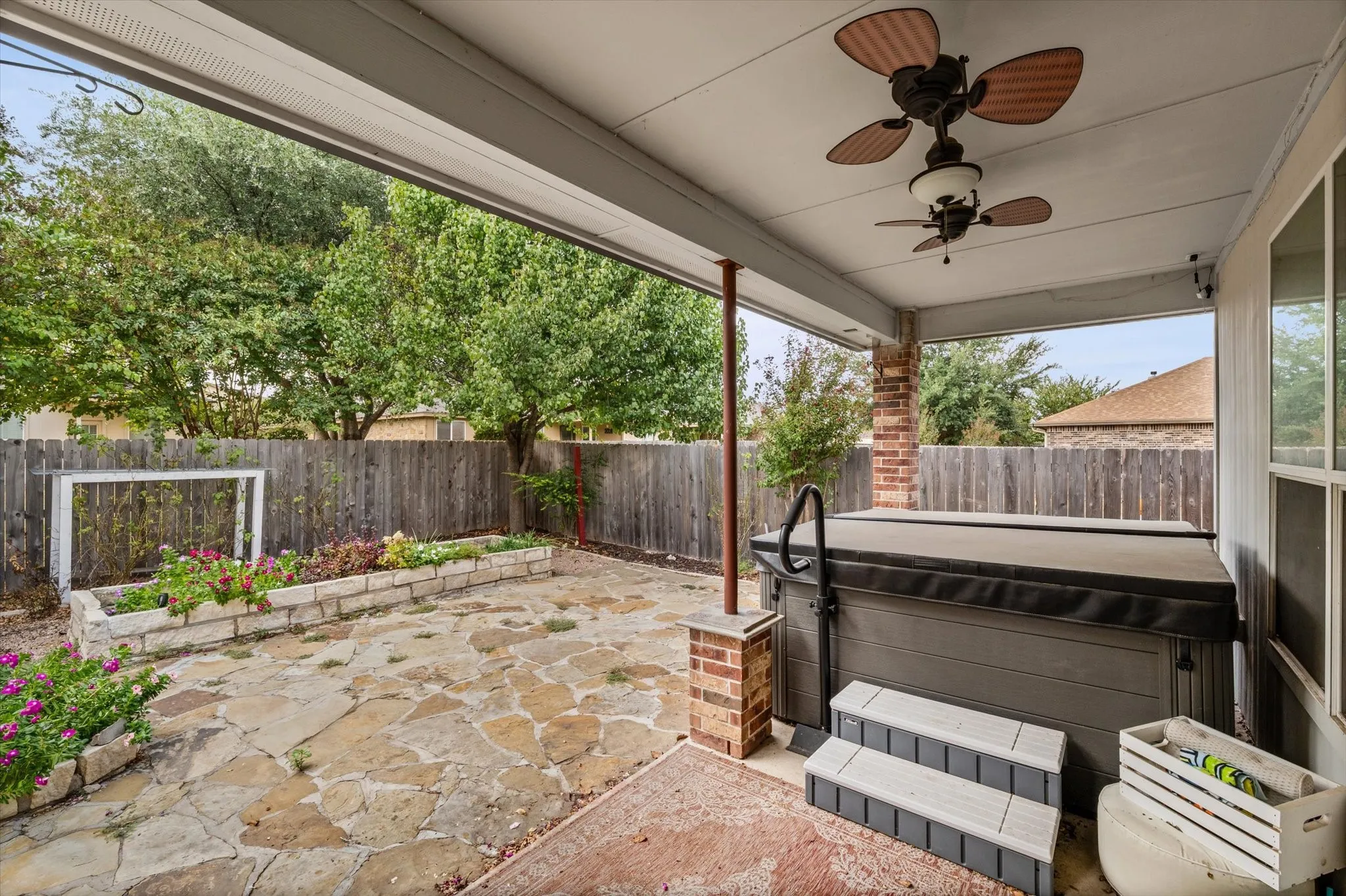 Covered patio with exposed brick support column, dual ceiling fans, and a built-in hot tub