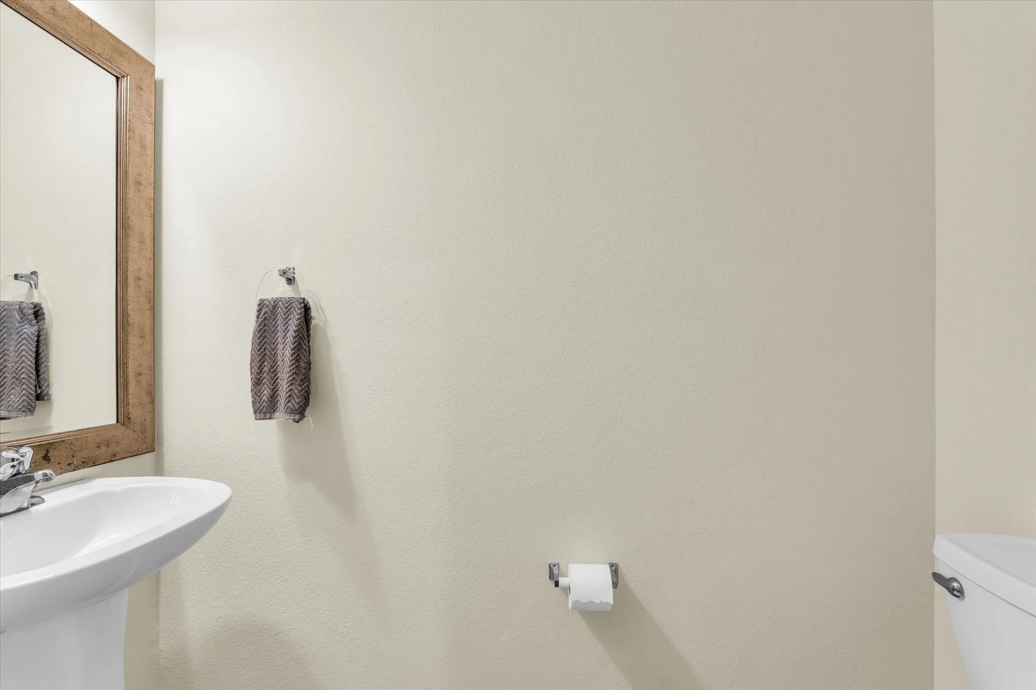 Pedestal sink, chrome faucet, wood-framed mirror, and chrome towel ring