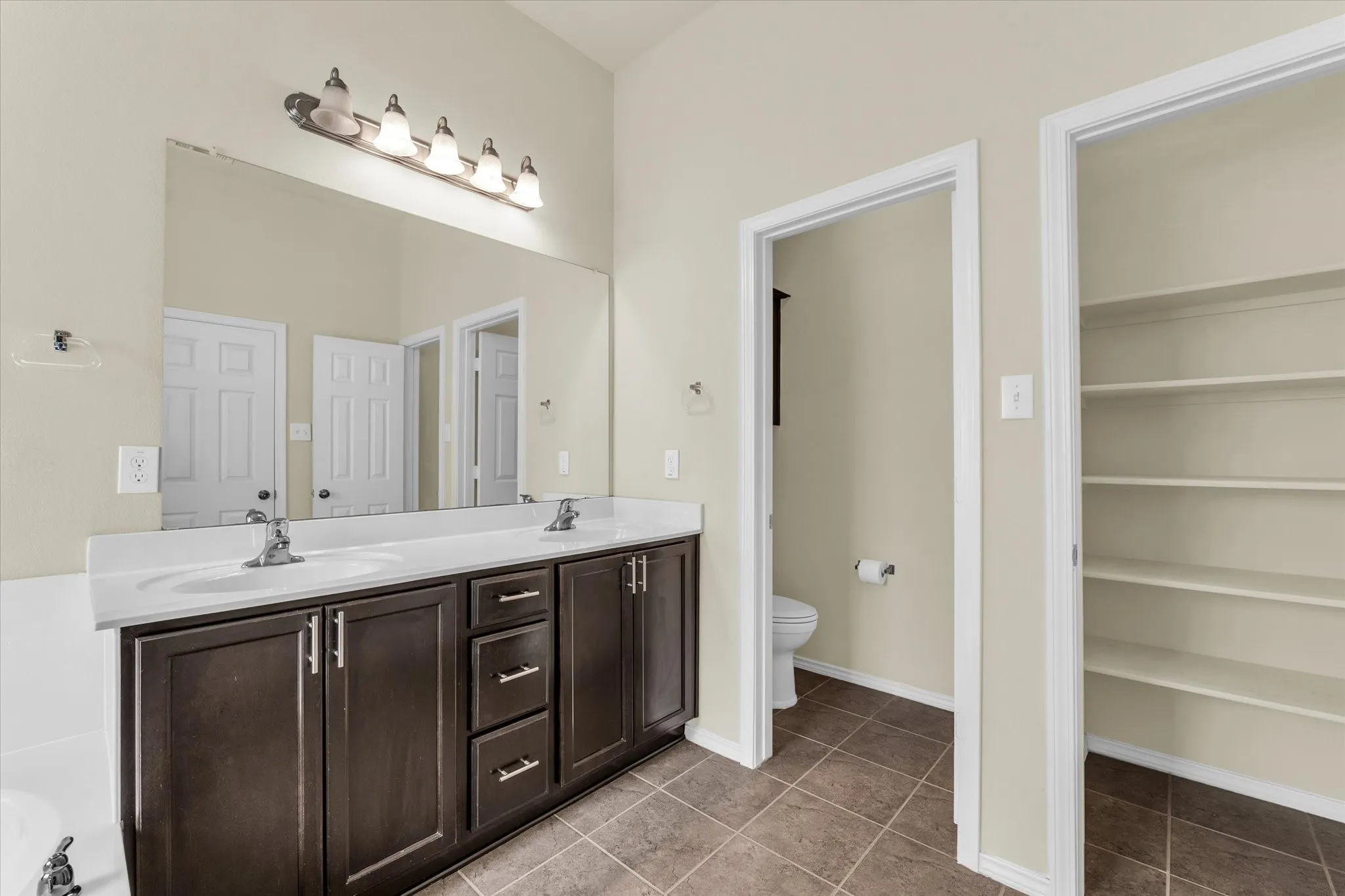 Dual vanity with white countertop, dark wood-finish cabinetry, a large wall-mounted mirror, and tile flooring
