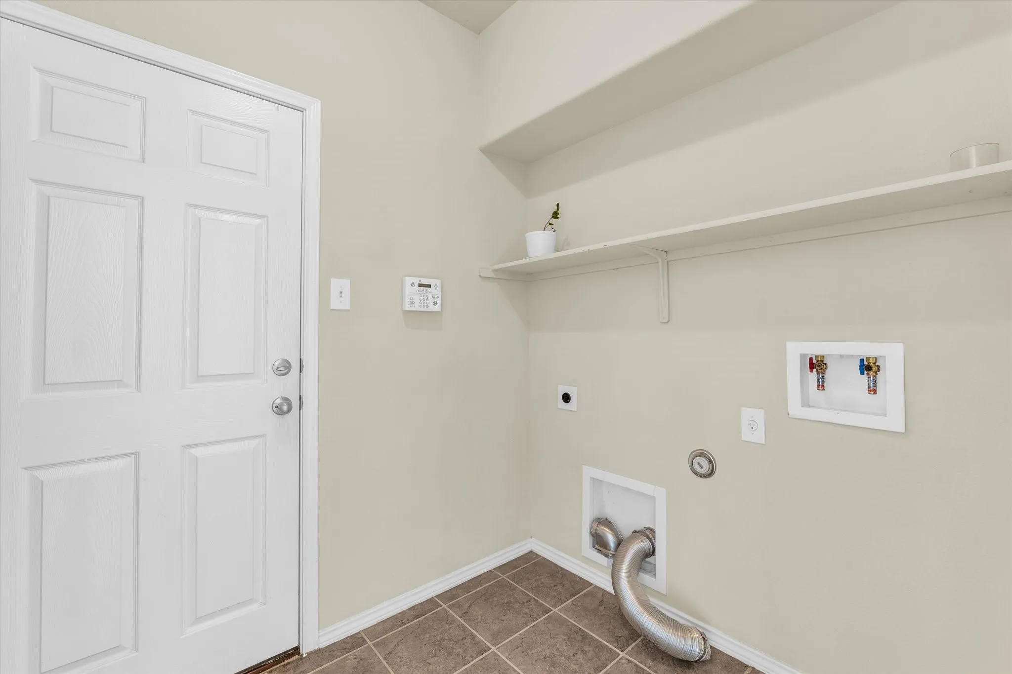 Utility space featuring tiled flooring, a white paneled door, wall-mounted shelving, and laundry hookups