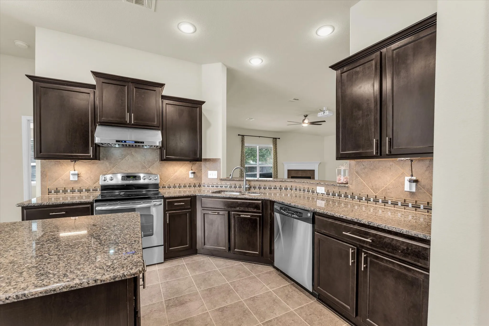 Kitchen featuring dark wood cabinetry, granite countertops, stainless steel appliances, tile backsplash, and recessed lighting