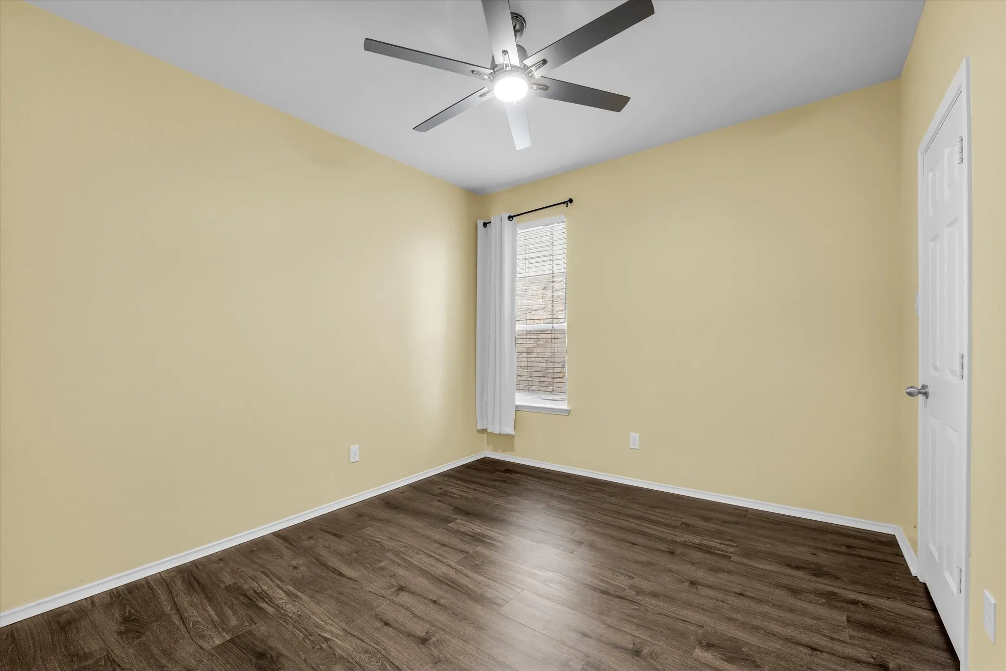 Wood-finish flooring, ceiling fan with integrated lighting, white trim, and a window with blinds