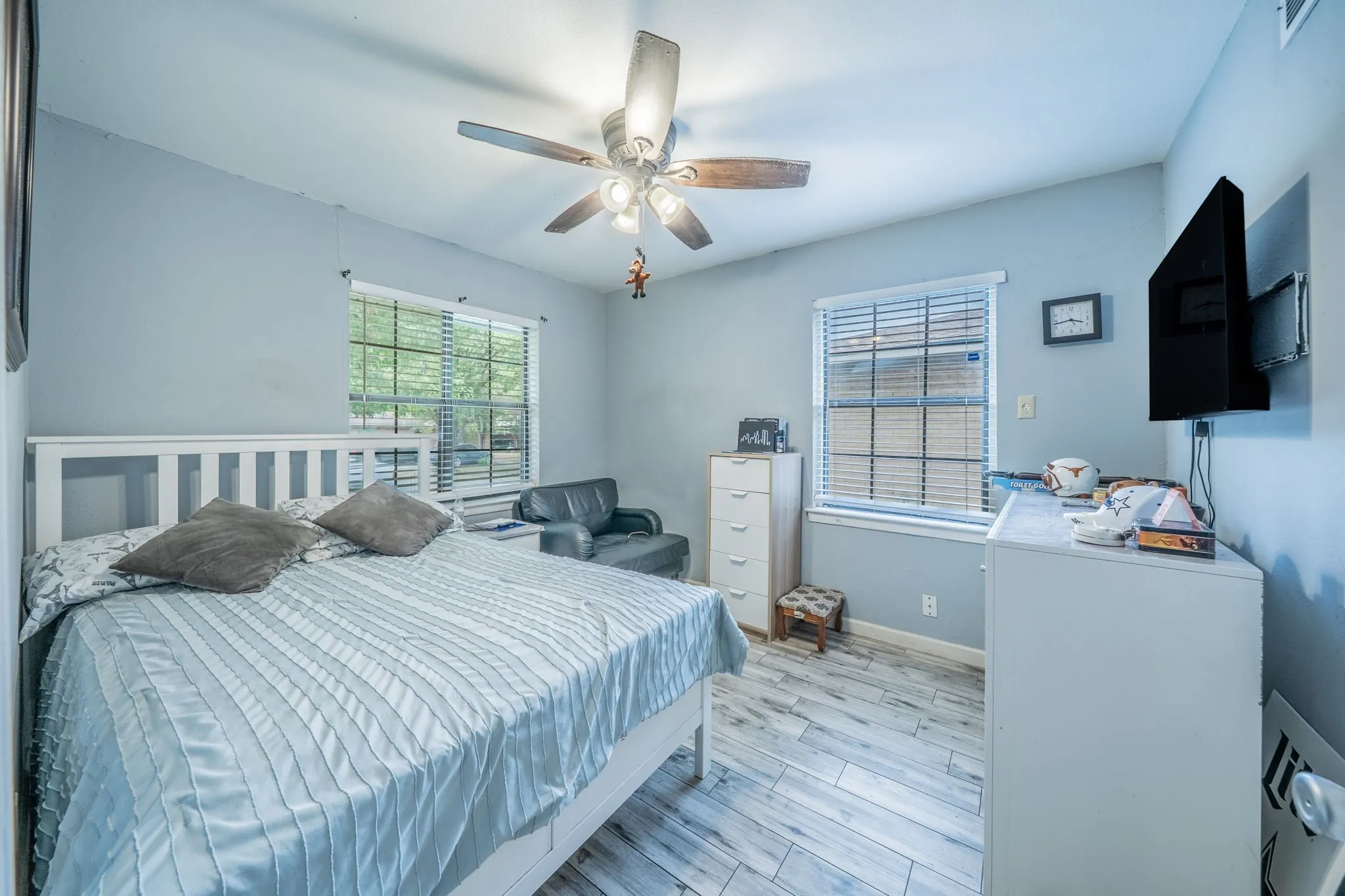 Wood-finish flooring with a ceiling fan light fixture and multiple windows with blinds