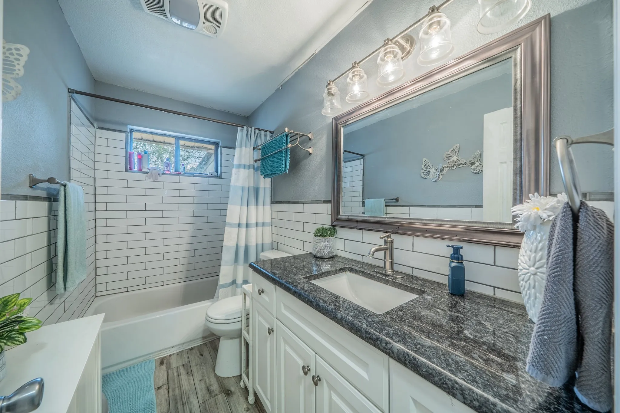 Bathroom with subway tile tub surround, white vanity, dark stone-finish countertop, undermount sink, and wood-finish flooring
