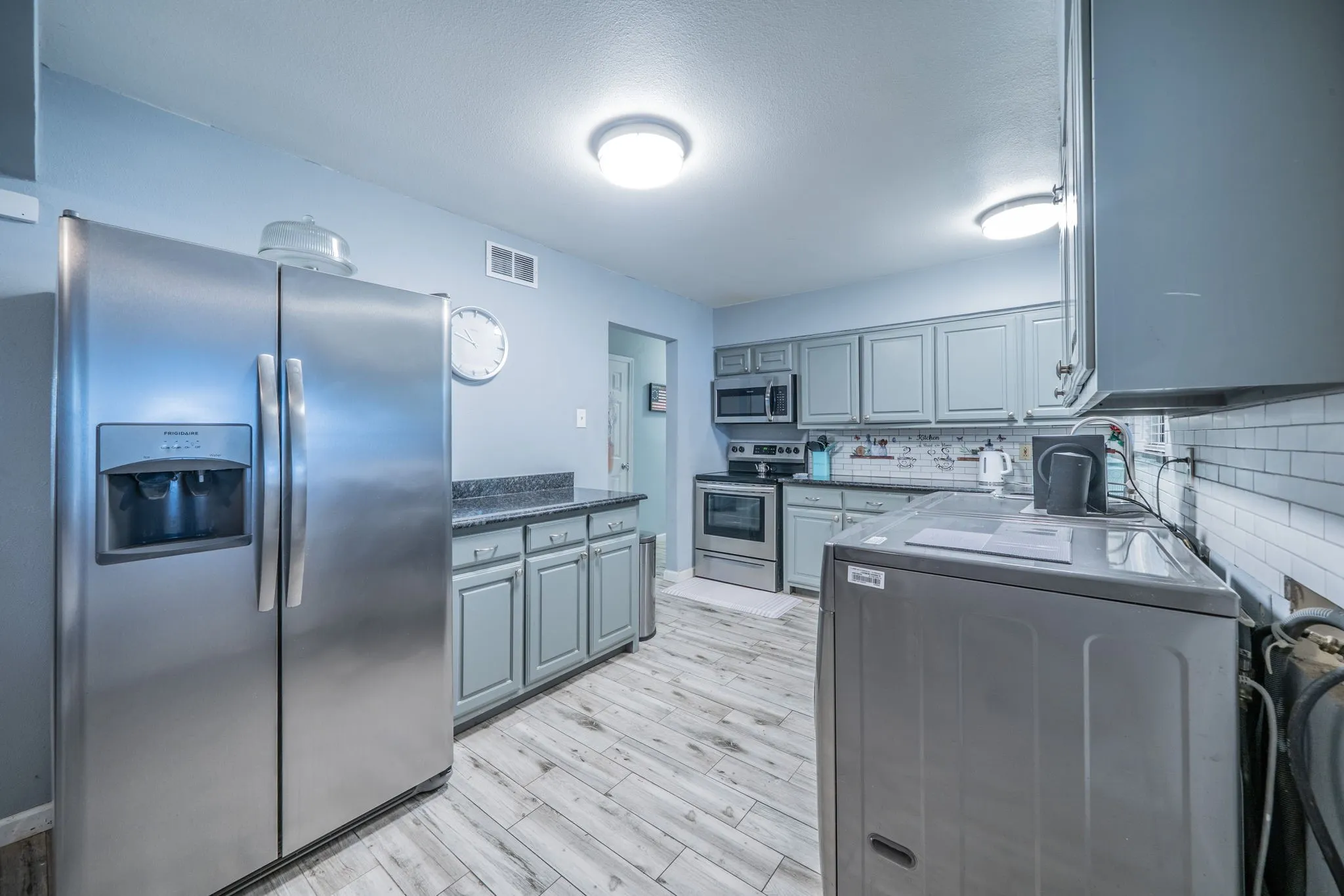 Kitchen featuring stainless steel appliances, wood-finish flooring, gray cabinetry, dark countertops, and a subway tile backsplash