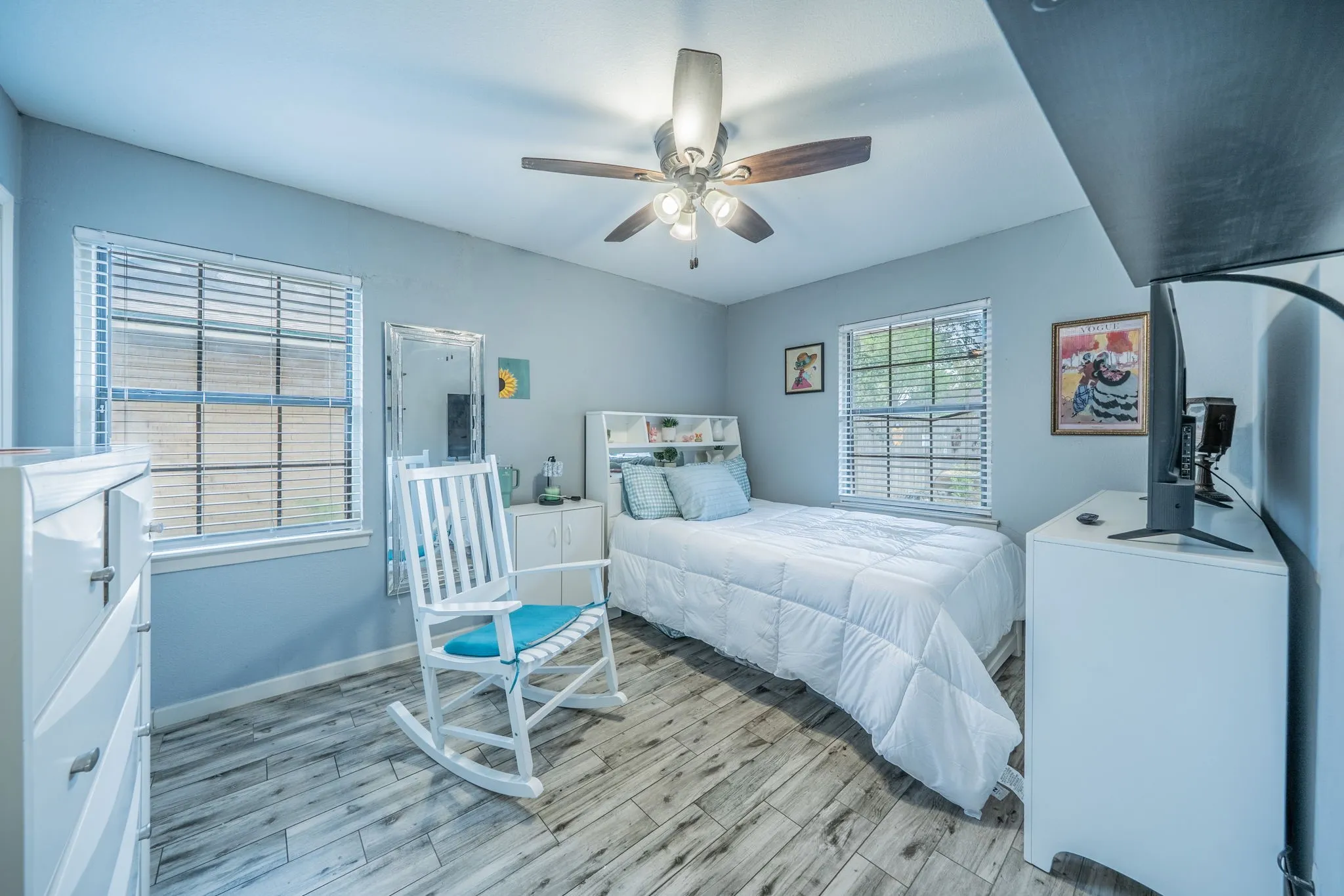 Wood-finish flooring, two windows with blinds, and a ceiling fan with light fixture