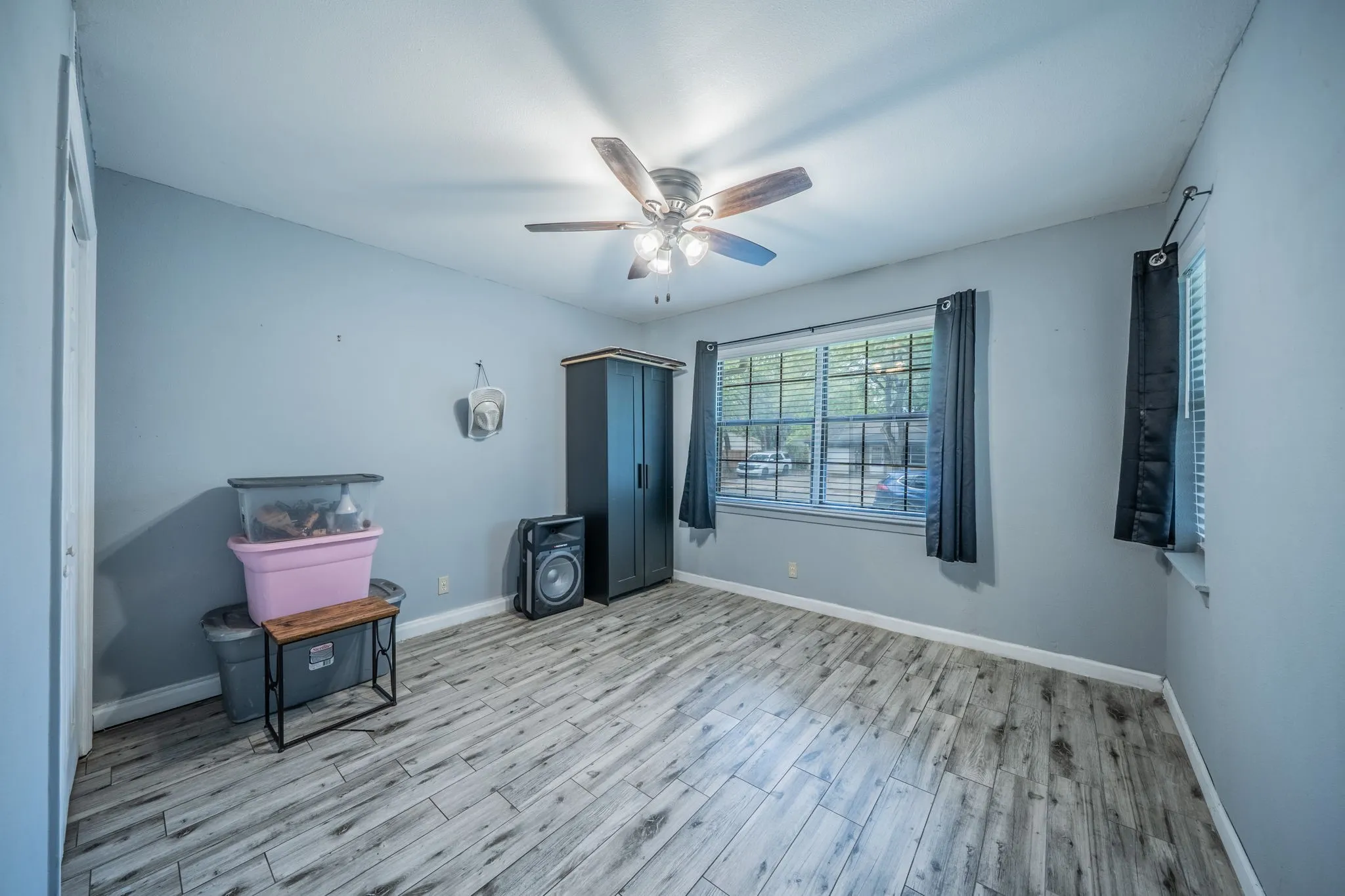 Recessed window with blinds, ceiling fan with light fixture, wood-finish flooring, and light-toned walls