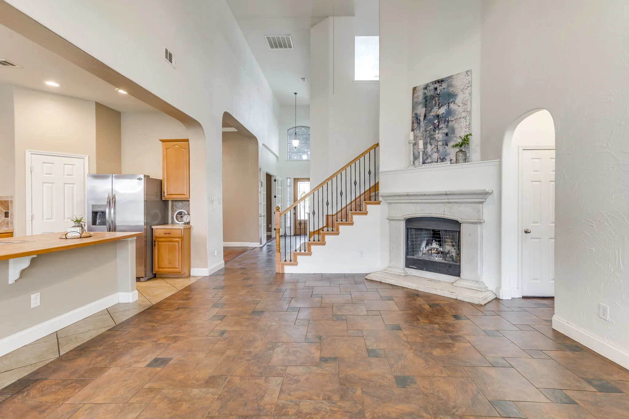 Soaring ceilings, a stone-surround fireplace, and a wood staircase with iron balusters define this open-concept space
