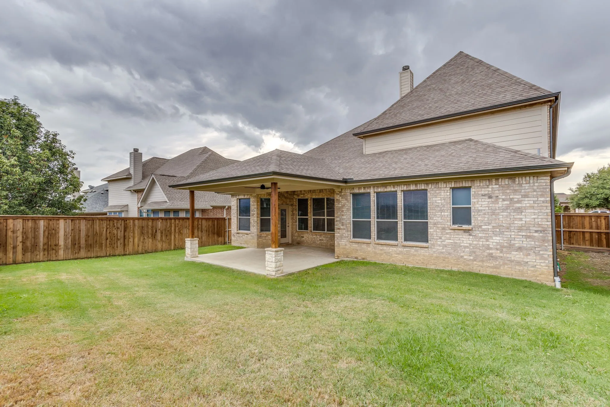 Expansive backyard featuring a covered patio with ceiling fans, a wooden privacy fence, and a brick exterior