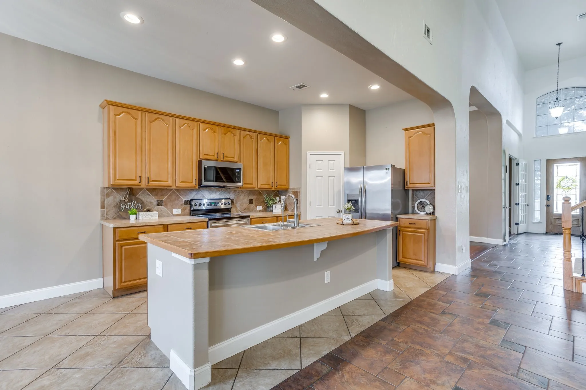 Kitchen featuring wood cabinetry, stainless steel appliances, a center island with an integrated sink, and a tiled backsplash