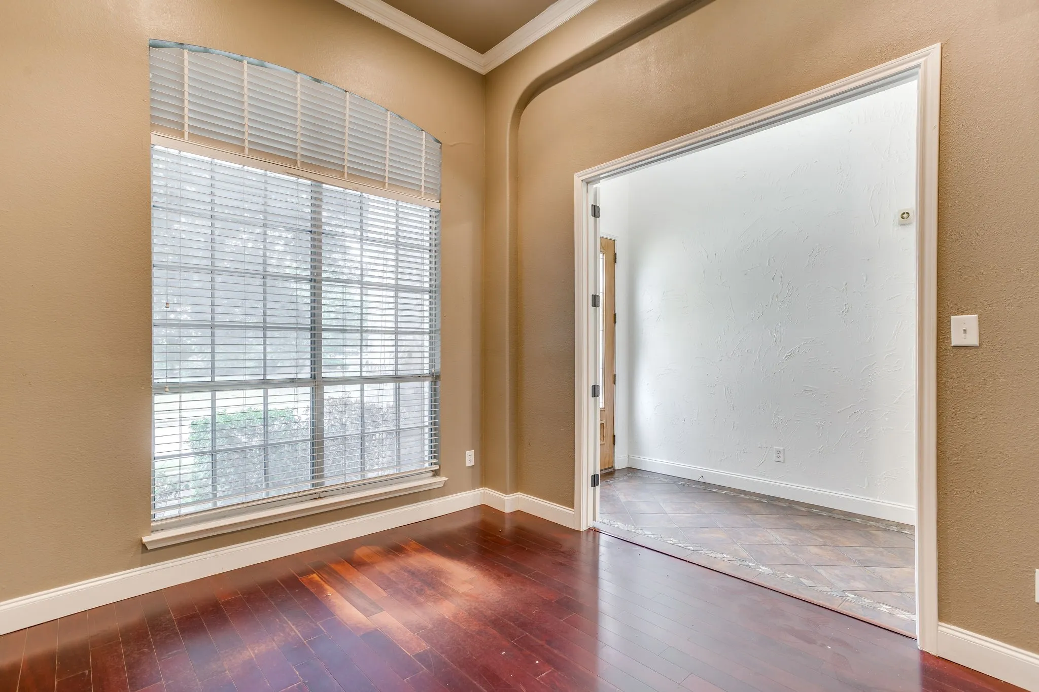 Arched window with blinds, wood-finish flooring, crown molding, and a wide entryway