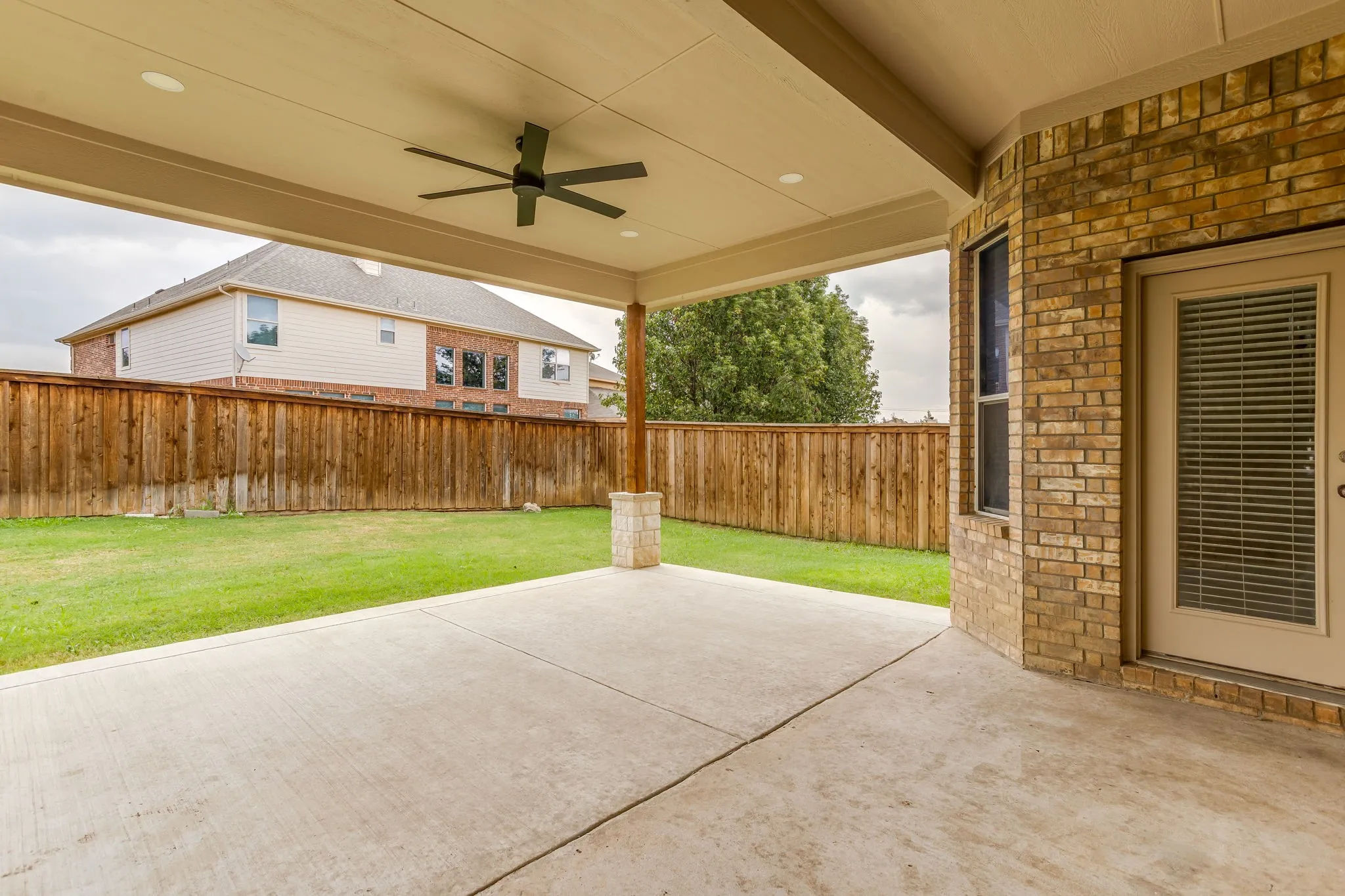 Expansive backyard featuring a covered patio with ceiling fans, a wooden privacy fence, and a brick exterior