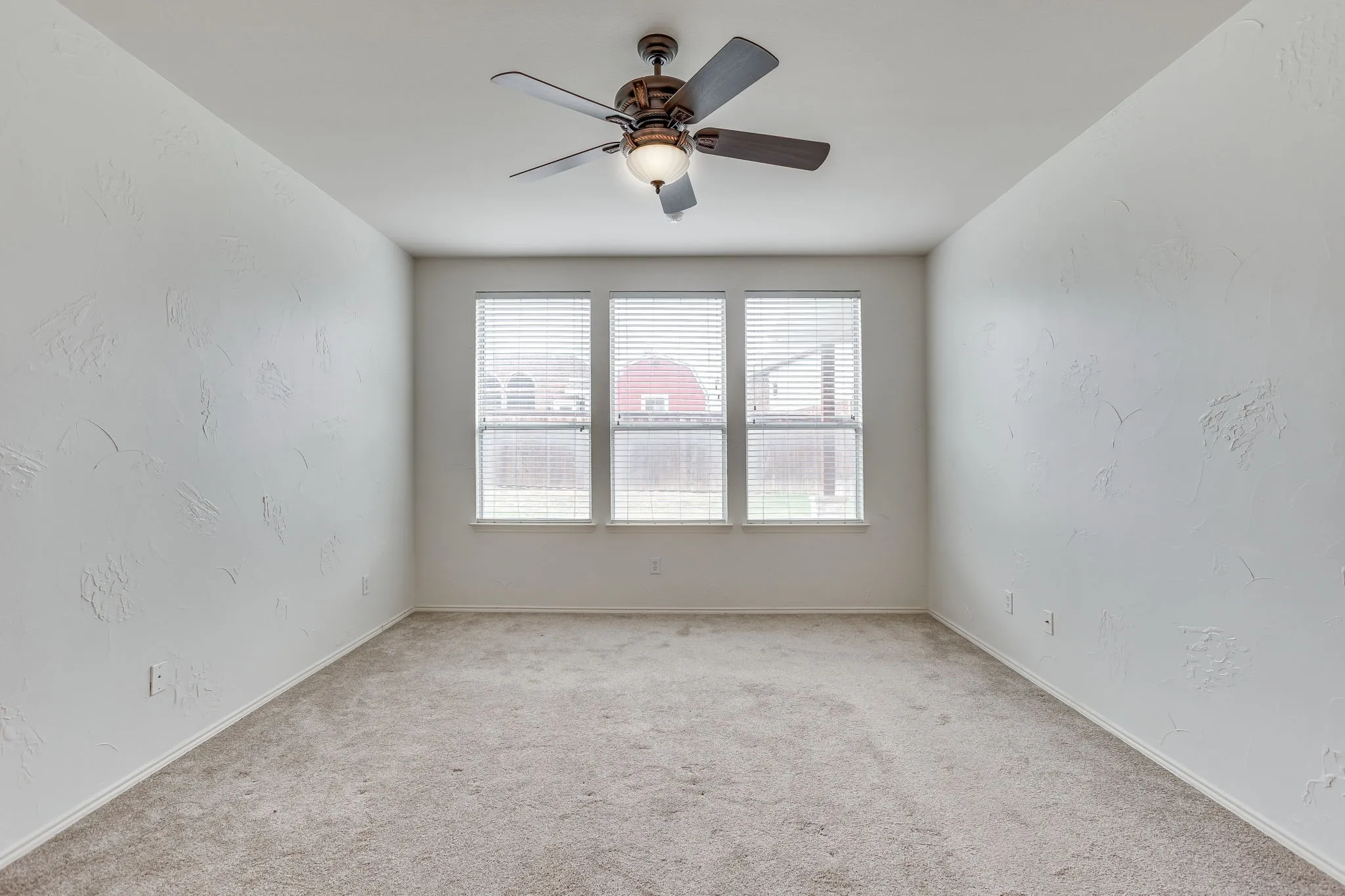 Bright and spacious bedroom featuring neutral wall finishes, abundant natural light from a large window with horizontal blinds, soft carpeting