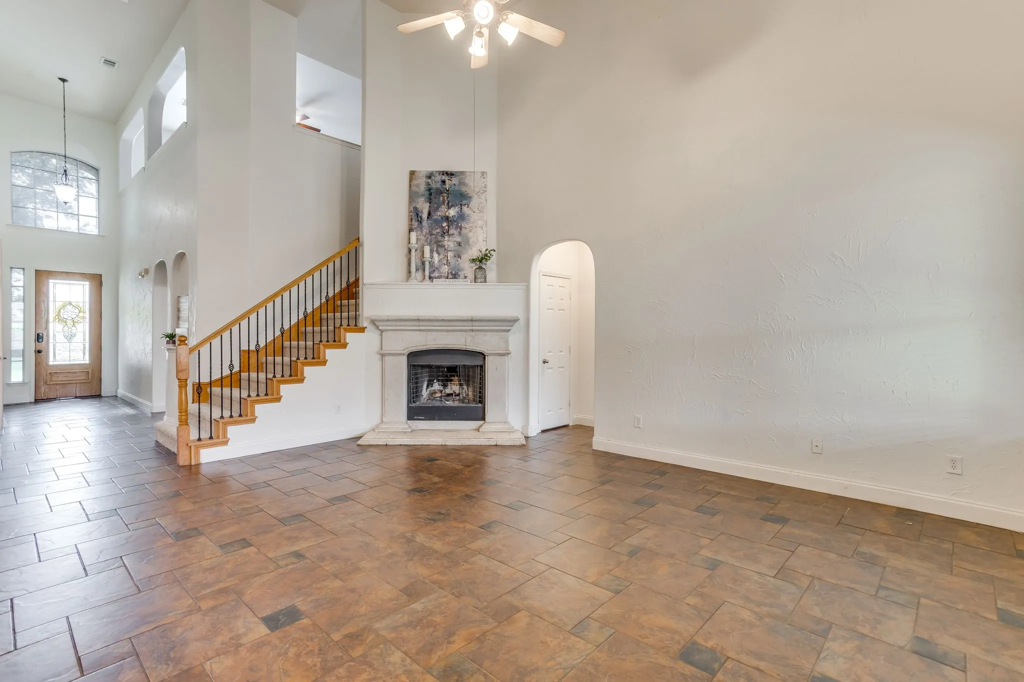 Two-story living area featuring a stone fireplace, wood and wrought iron staircase, high ceilings with a ceiling fan, and tile flooring