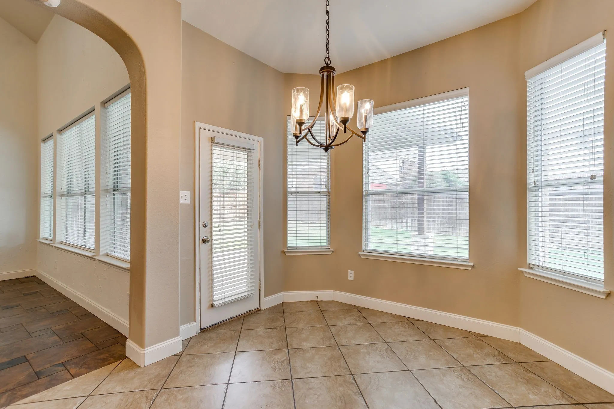 Bay window with horizontal blinds, overhead chandelier, and tile flooring