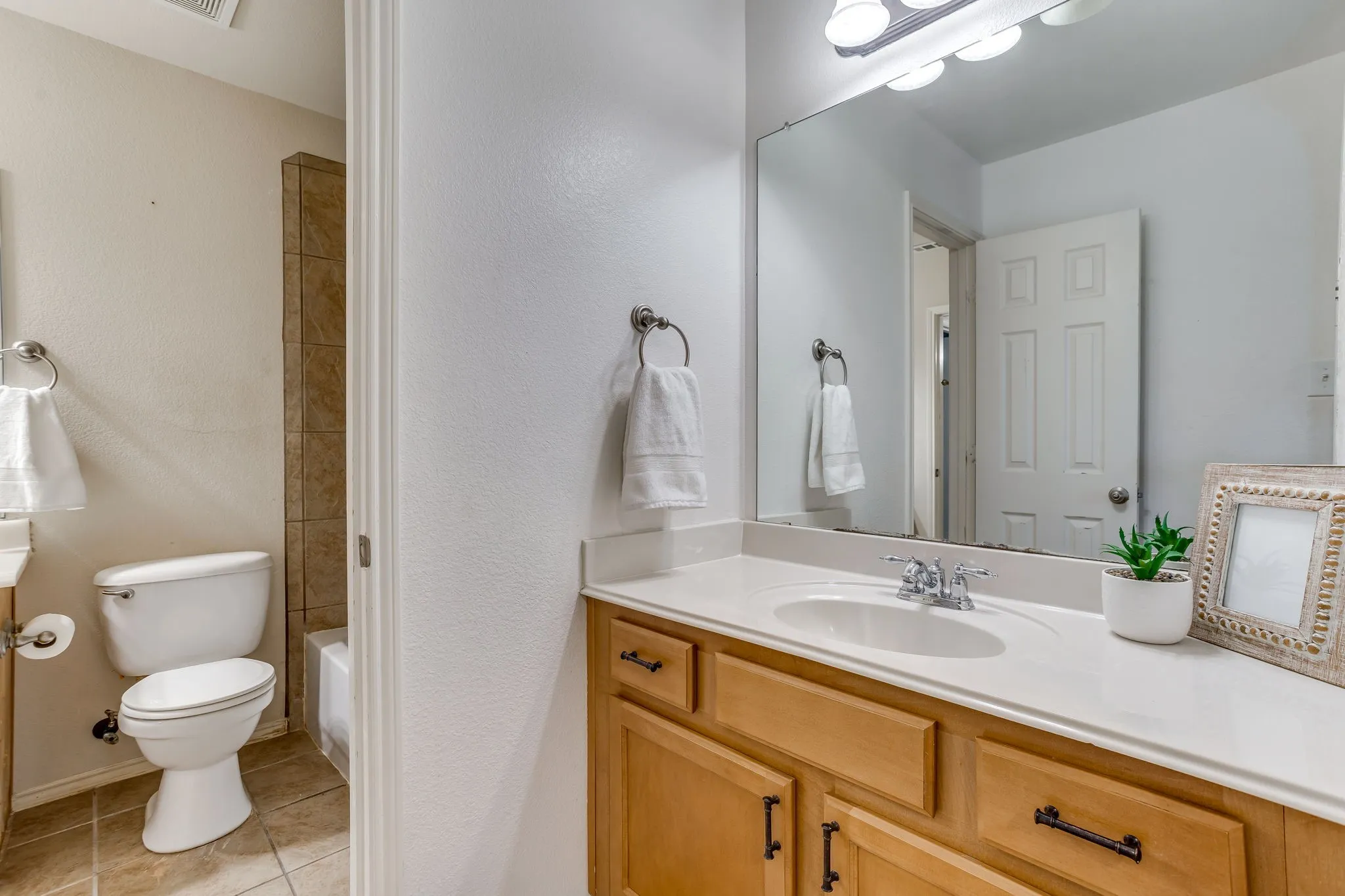 Vanity with wood-finish cabinetry, integrated sink, and a large wall-mounted mirror