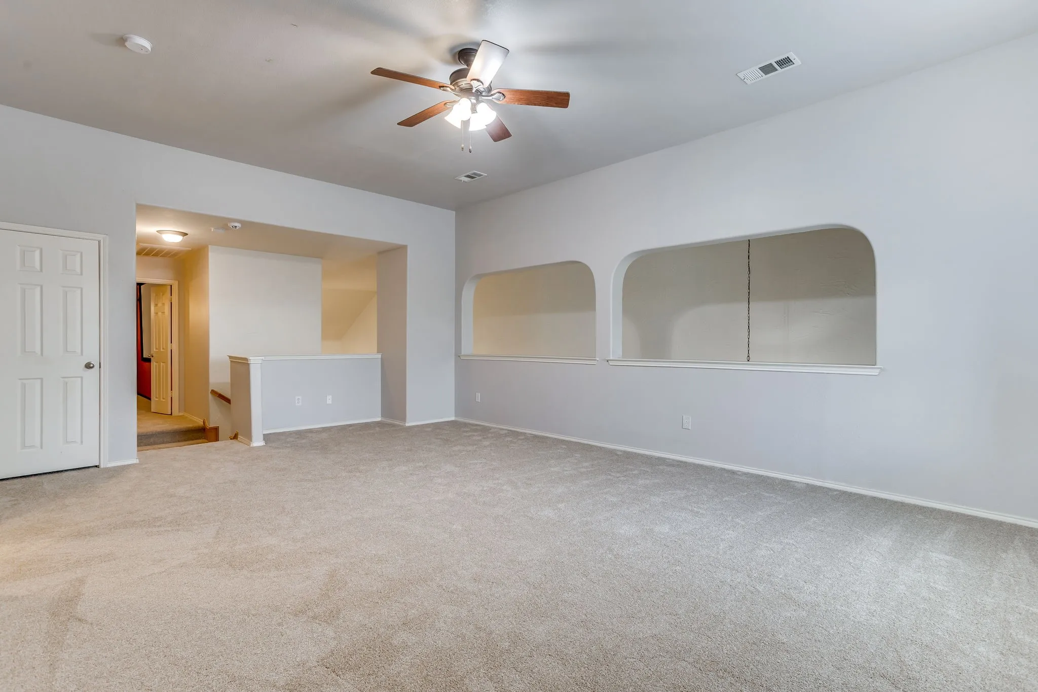 Expansive carpeted room featuring a ceiling fan, arched wall cutouts, and a white six-panel door