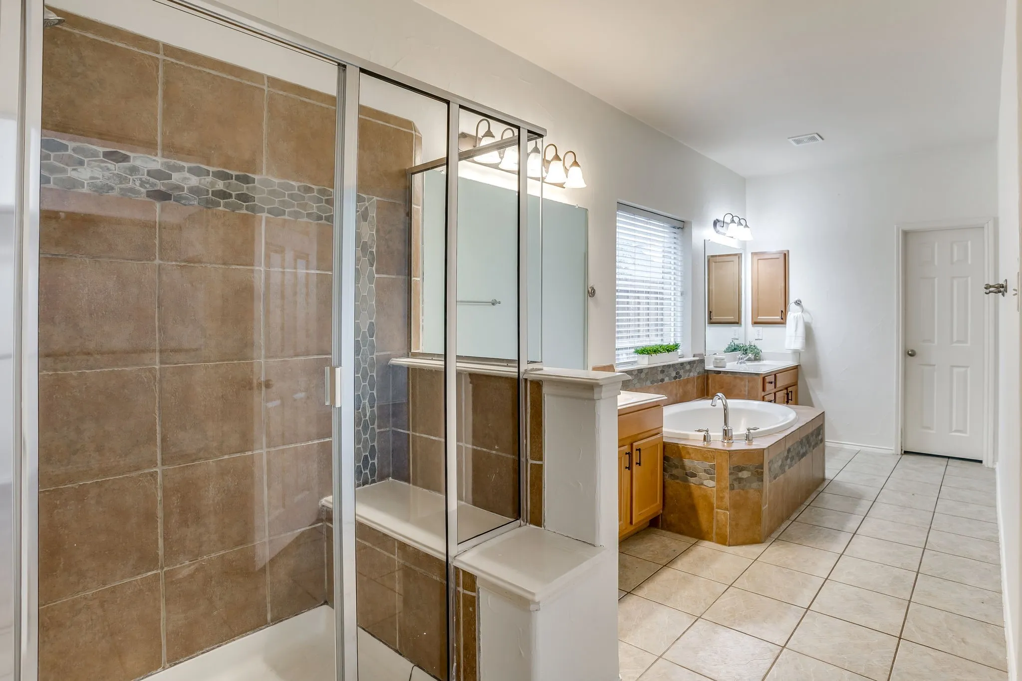 Spacious bathroom featuring a glass-enclosed shower, corner soaking tub, vanity with wood cabinetry, tile flooring, and neutral wall tones