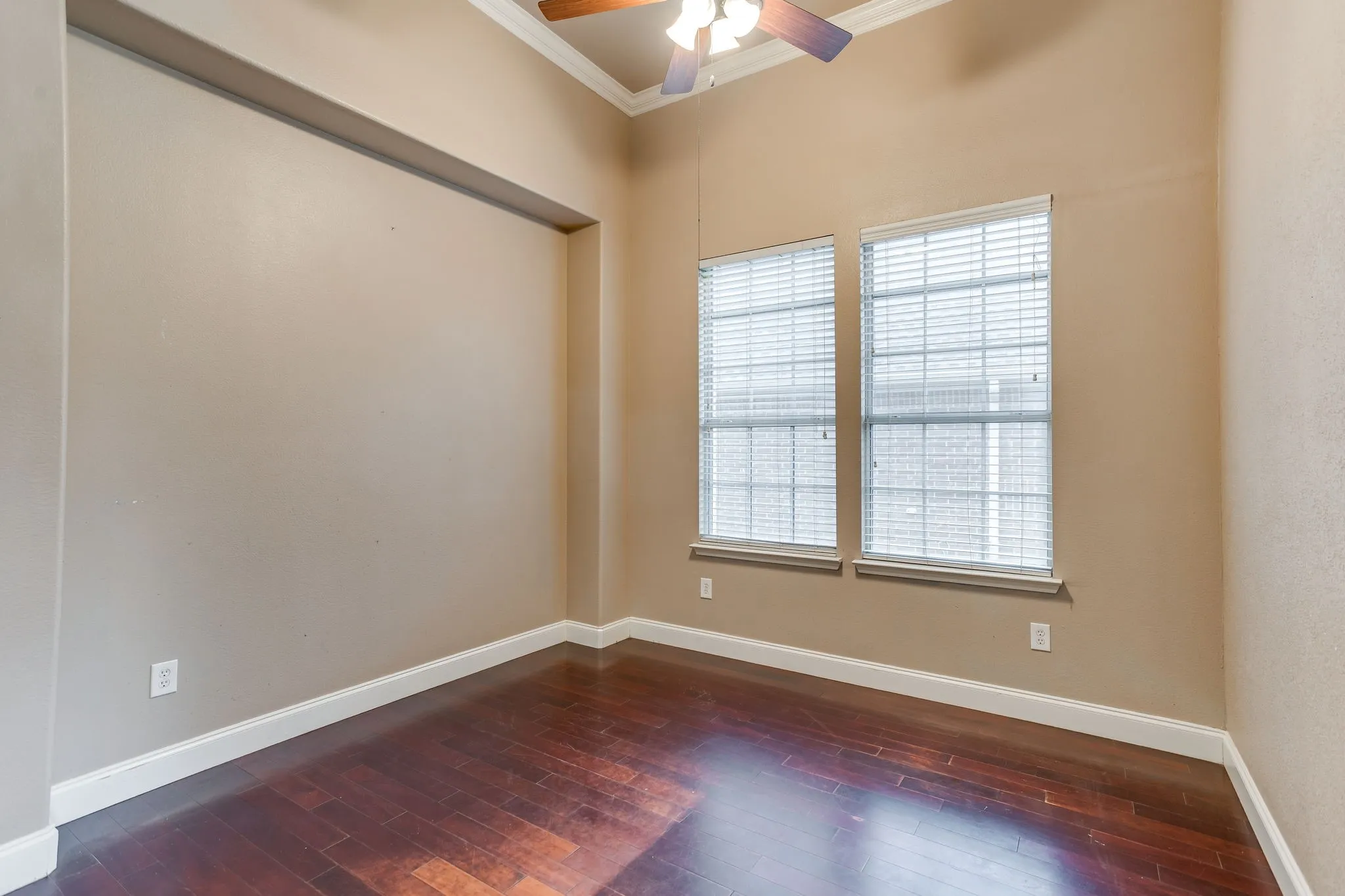 Rich wood-finish flooring, two large windows with blinds, ceiling fan, and recessed wall niche