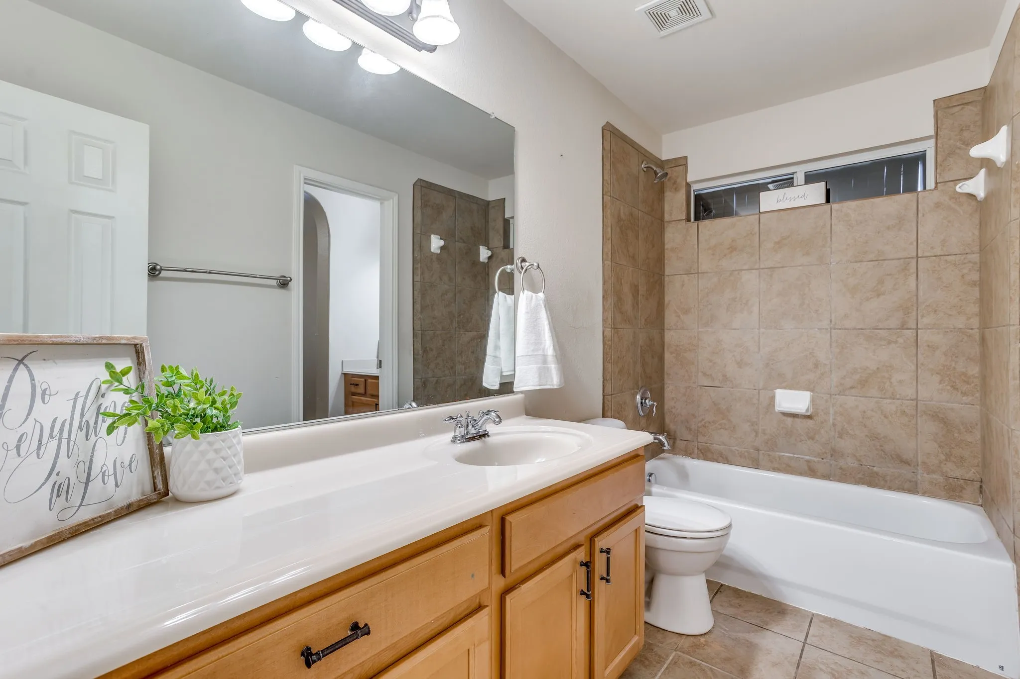 Bathroom featuring a light wood-finish vanity, integrated sink, and a large wall-mounted mirror