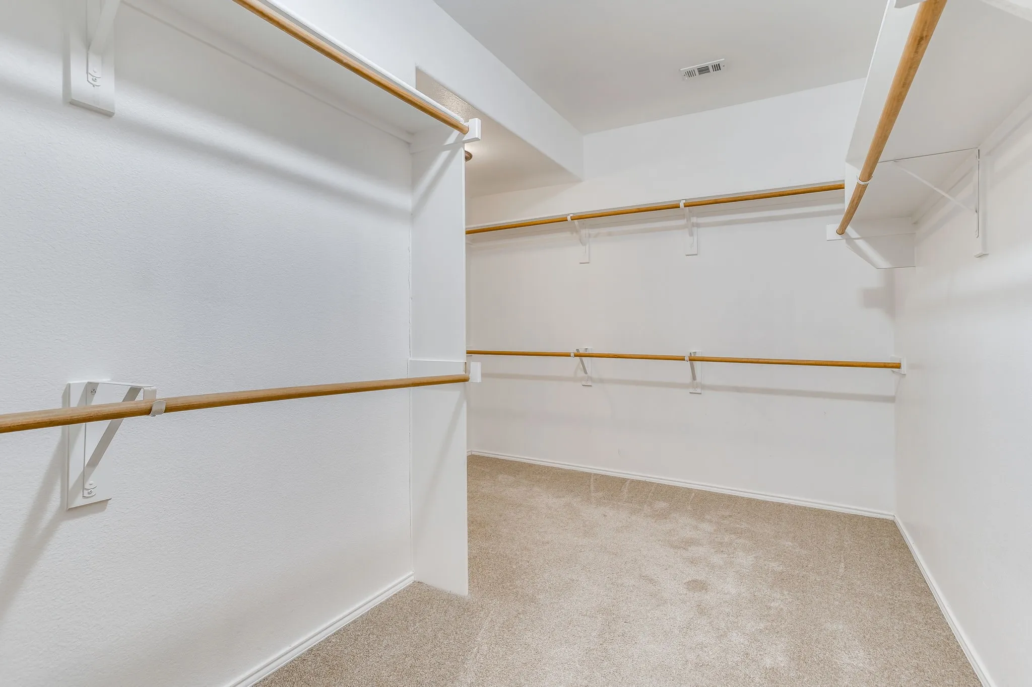 Walk-in closet featuring carpet flooring, multiple wooden hanging rods, and white walls