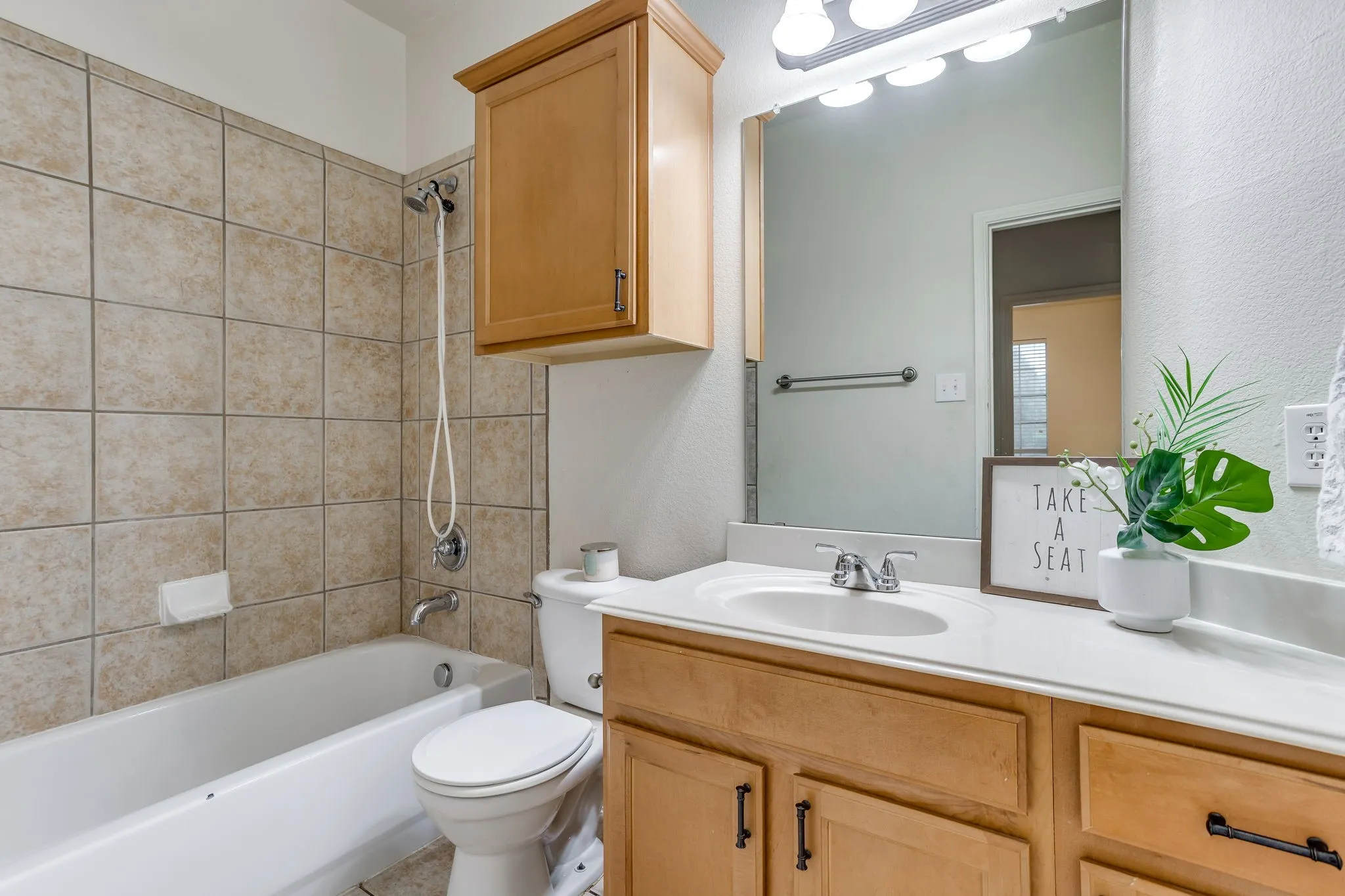 Bathroom featuring a vanity with a white countertop, wood-finish cabinetry, a built-in mirror, a tub/shower combination with tile surround, and an overhead storage cabinet