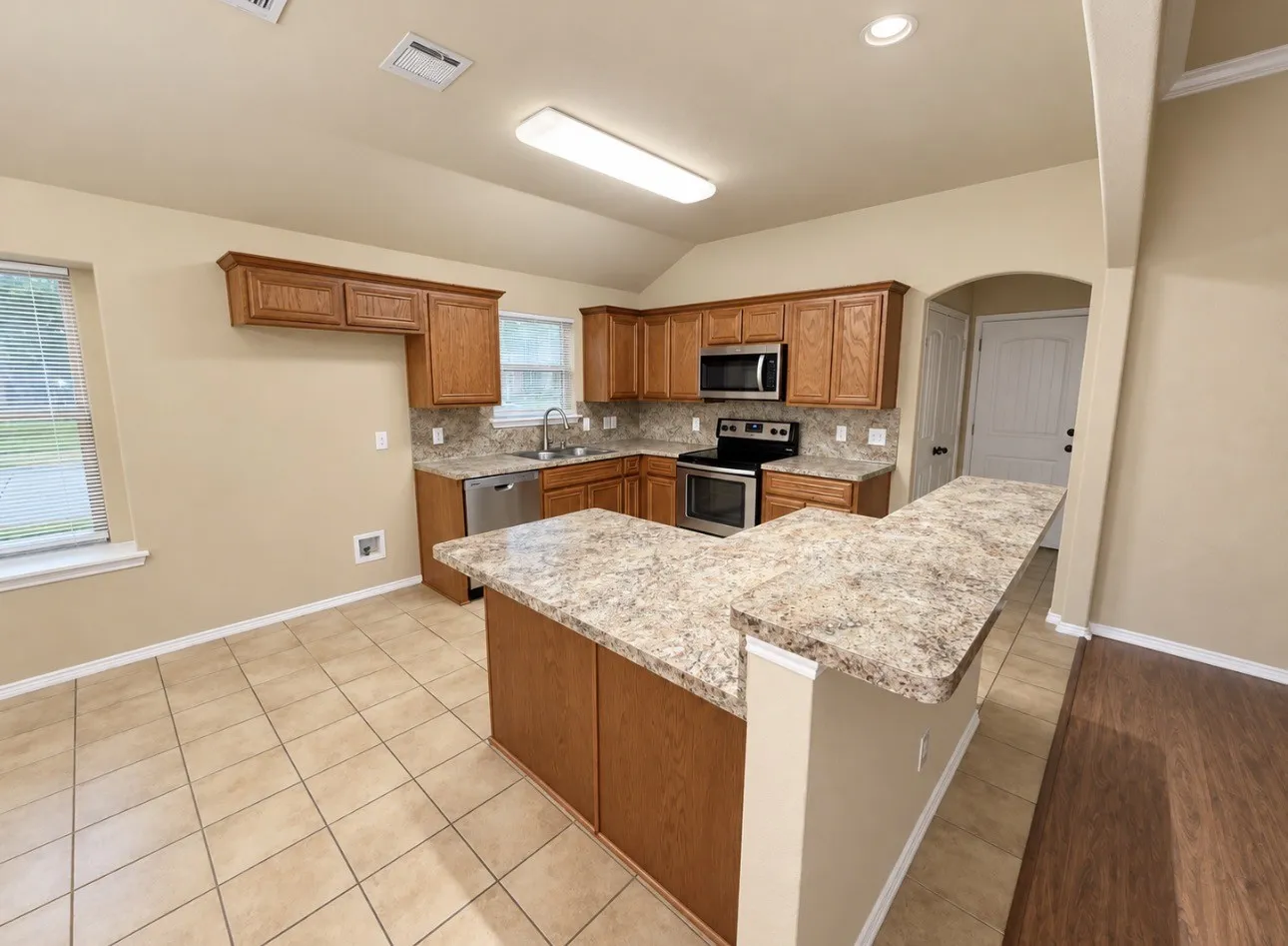 Kitchen featuring wood cabinetry, stone countertops, stainless steel appliances, tile flooring, and a breakfast bar
