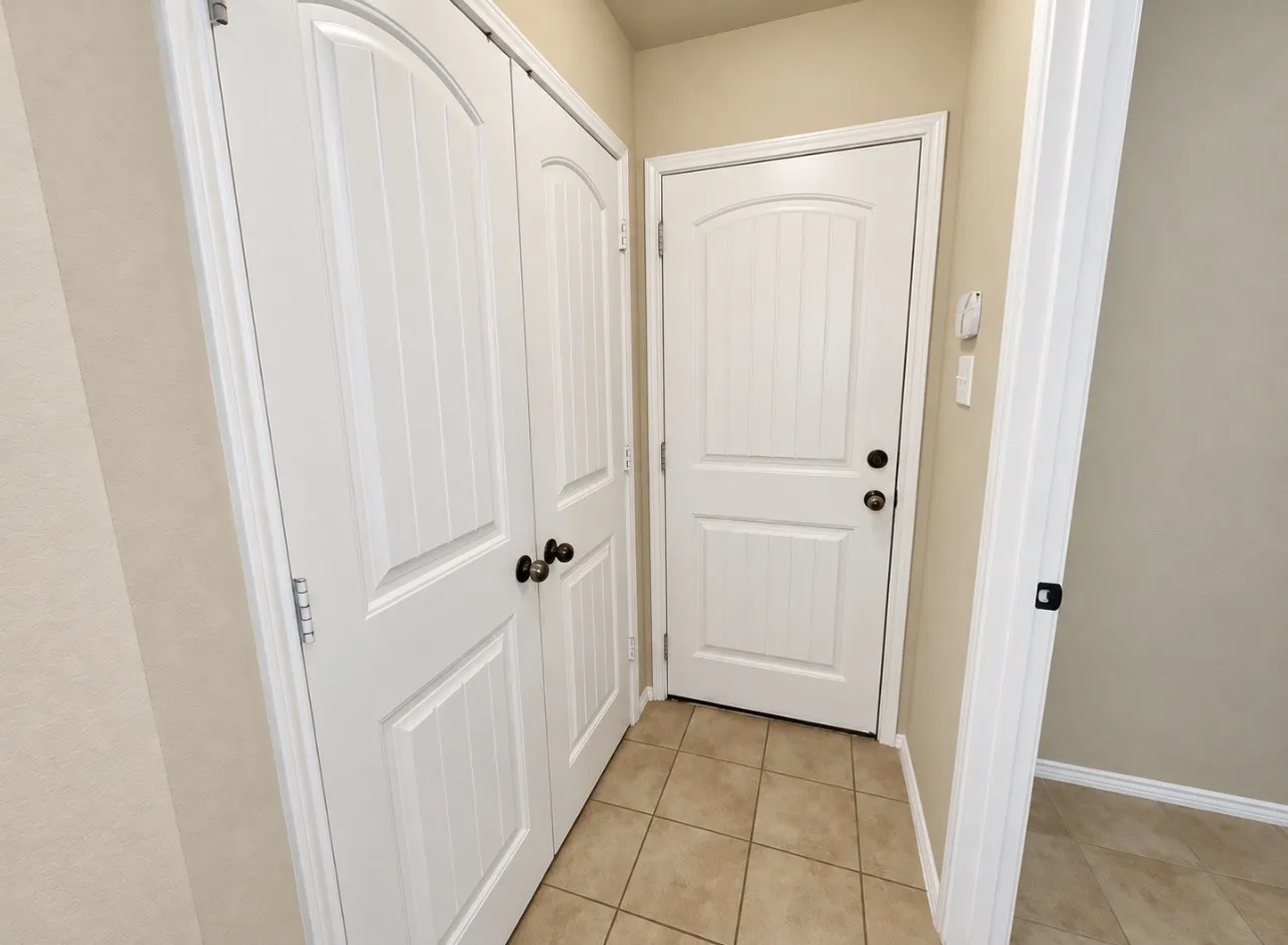 Paneled doors with arched detailing, black hardware, and tiled flooring